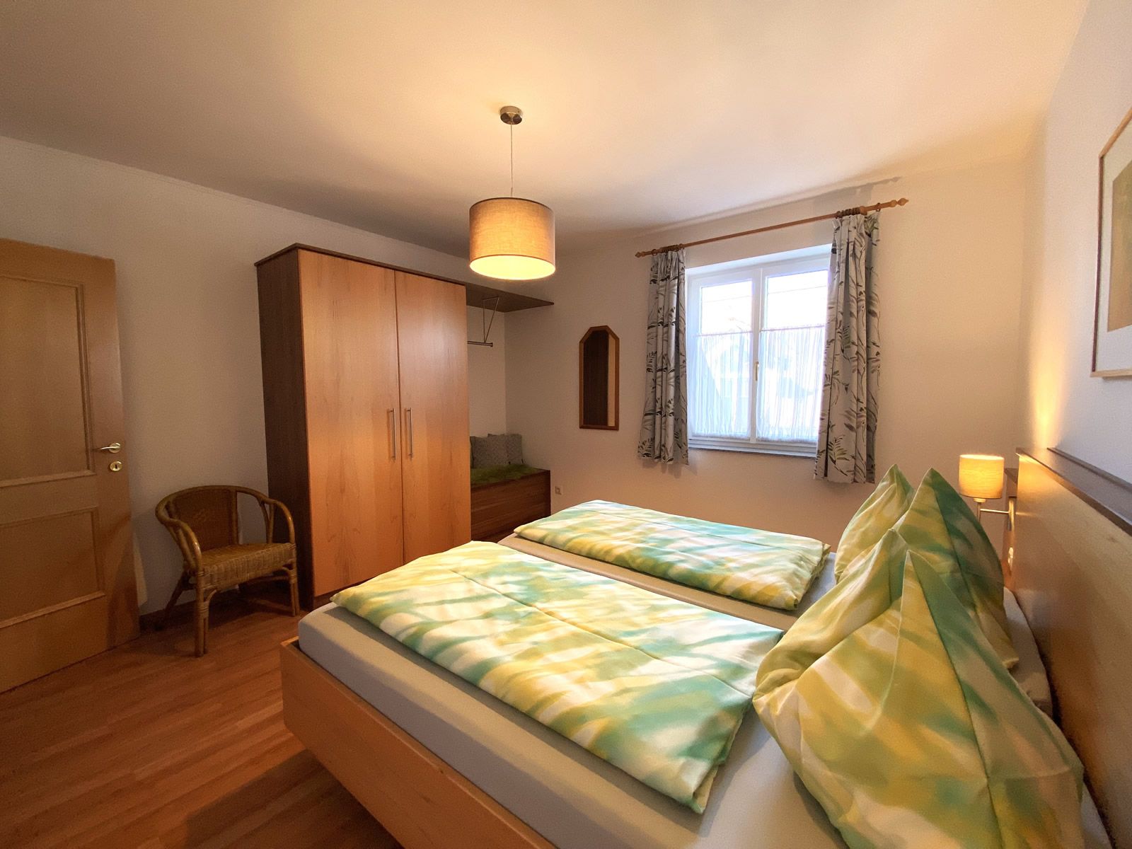 Ložnice s manželskou postelí, šatní skříní, židlí a oknem.