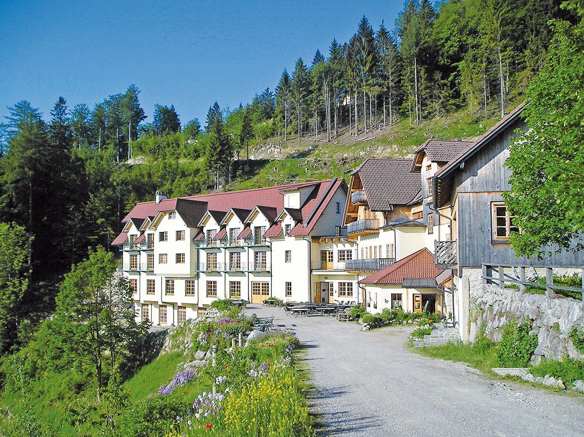 Velká budova s červenými střechami v zeleném zalesněném prostředí.