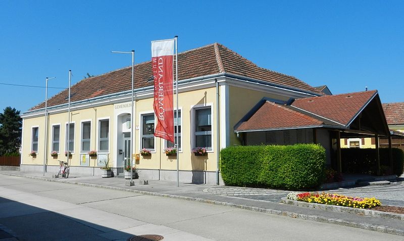 Obecní úřad v Rauchenwarthu, žlutá budova s červenou střechou a květinami.