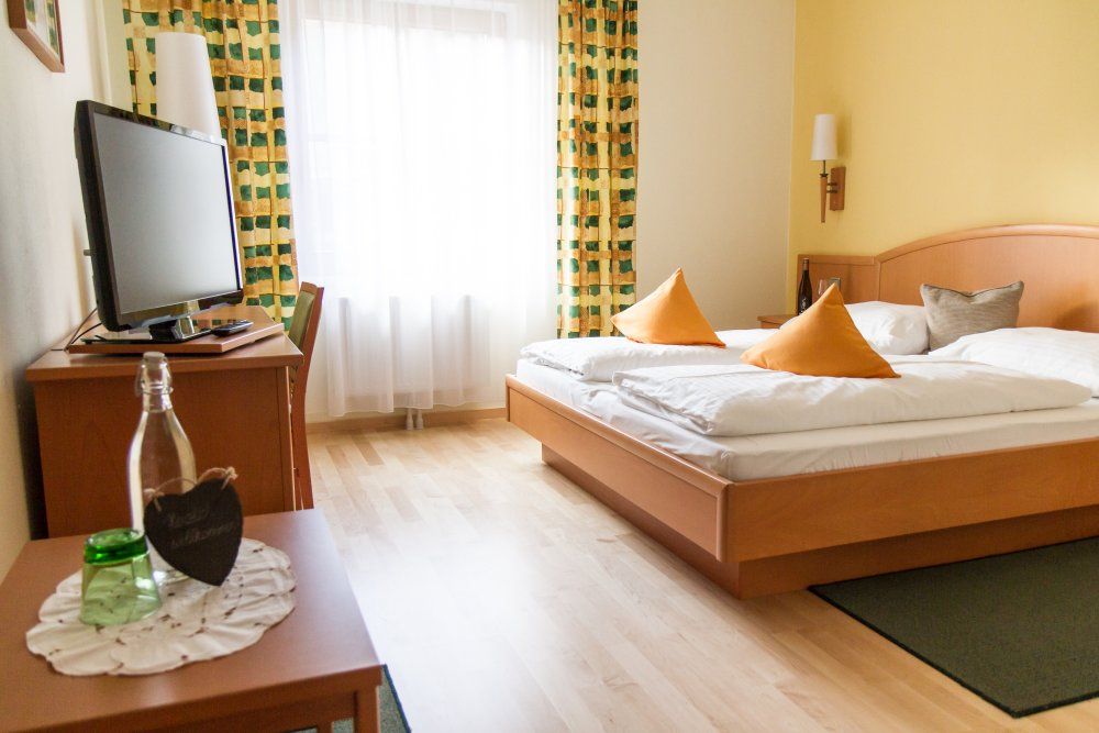 Útulný hotelový pokoj s manželskou postelí, TV a závěsy.