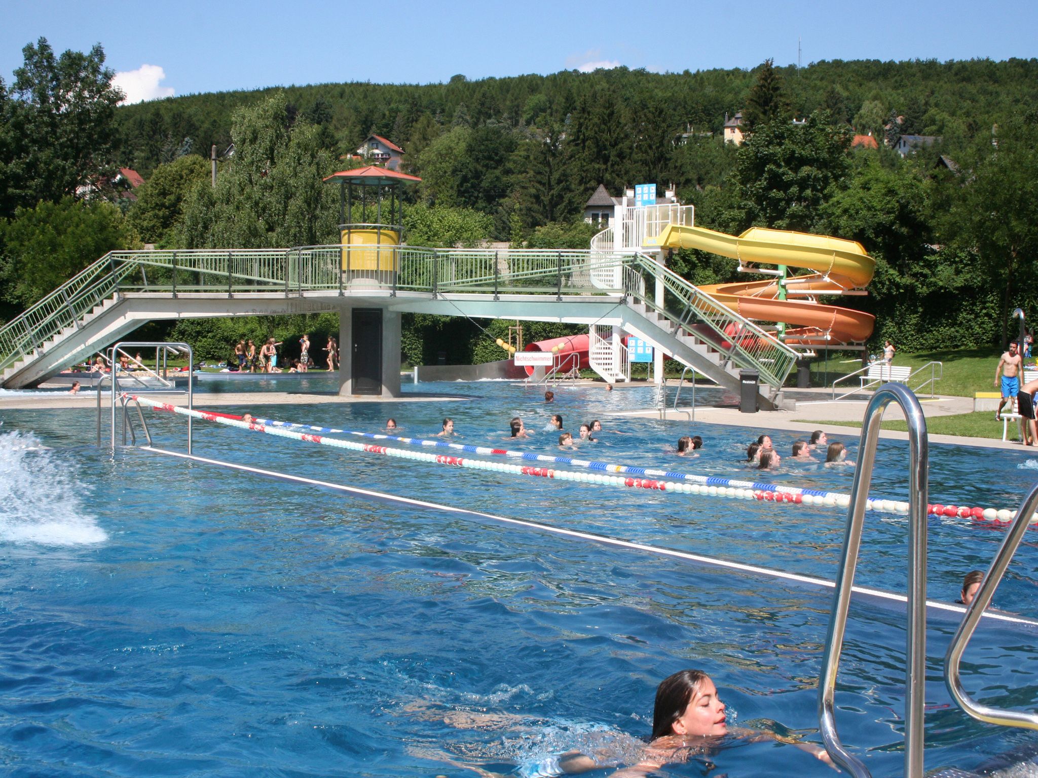 Venkovní bazén s plováky, skluzavkou a mostem v lázních Wienerwaldbad Purkersdorf.