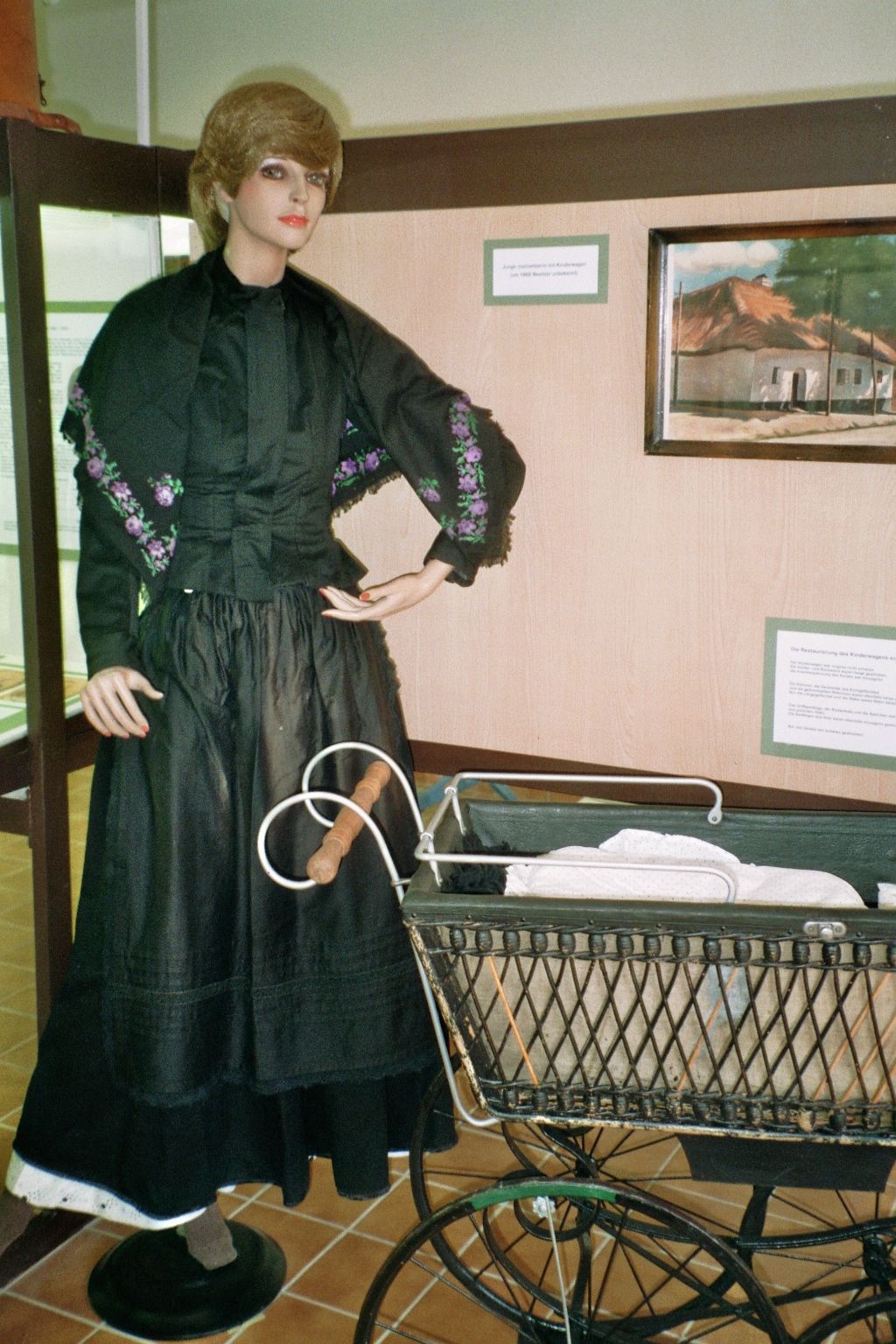 Figurína v tradičním oděvu vedle starého kočárku v showroomu.