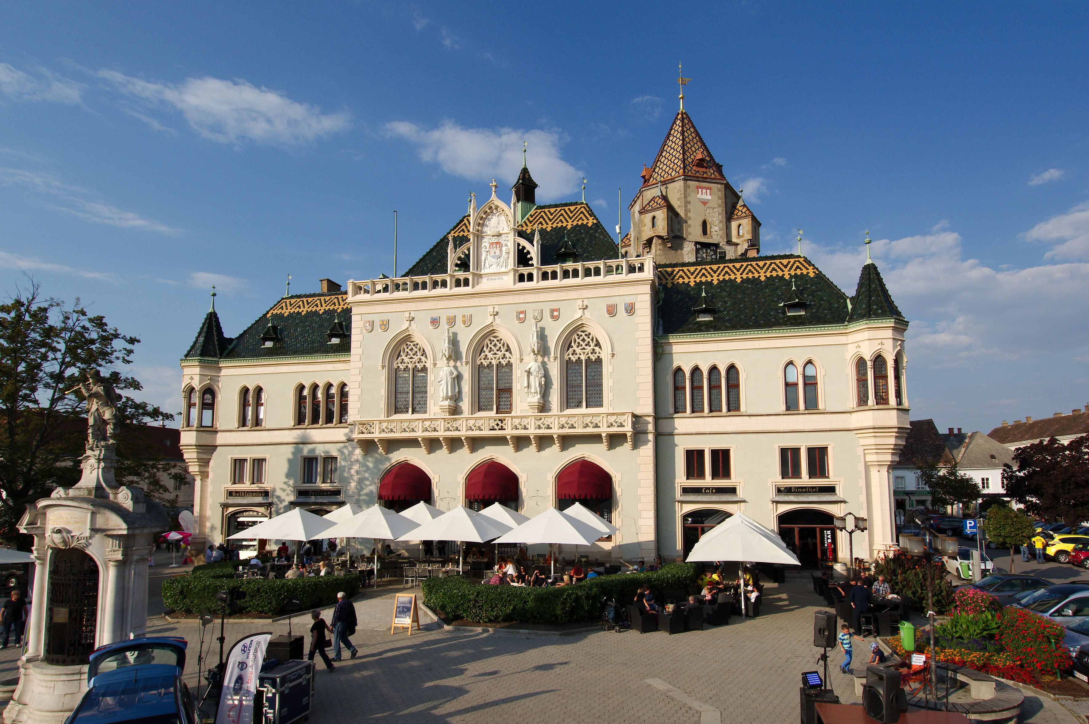 Korneuburská radnice s pozoruhodnou architekturou a slunečníky v popředí.