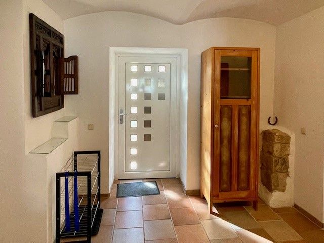 Vstupní prostor s bílými dveřmi, dřevěnou skříní a dlážděnou podlahou.