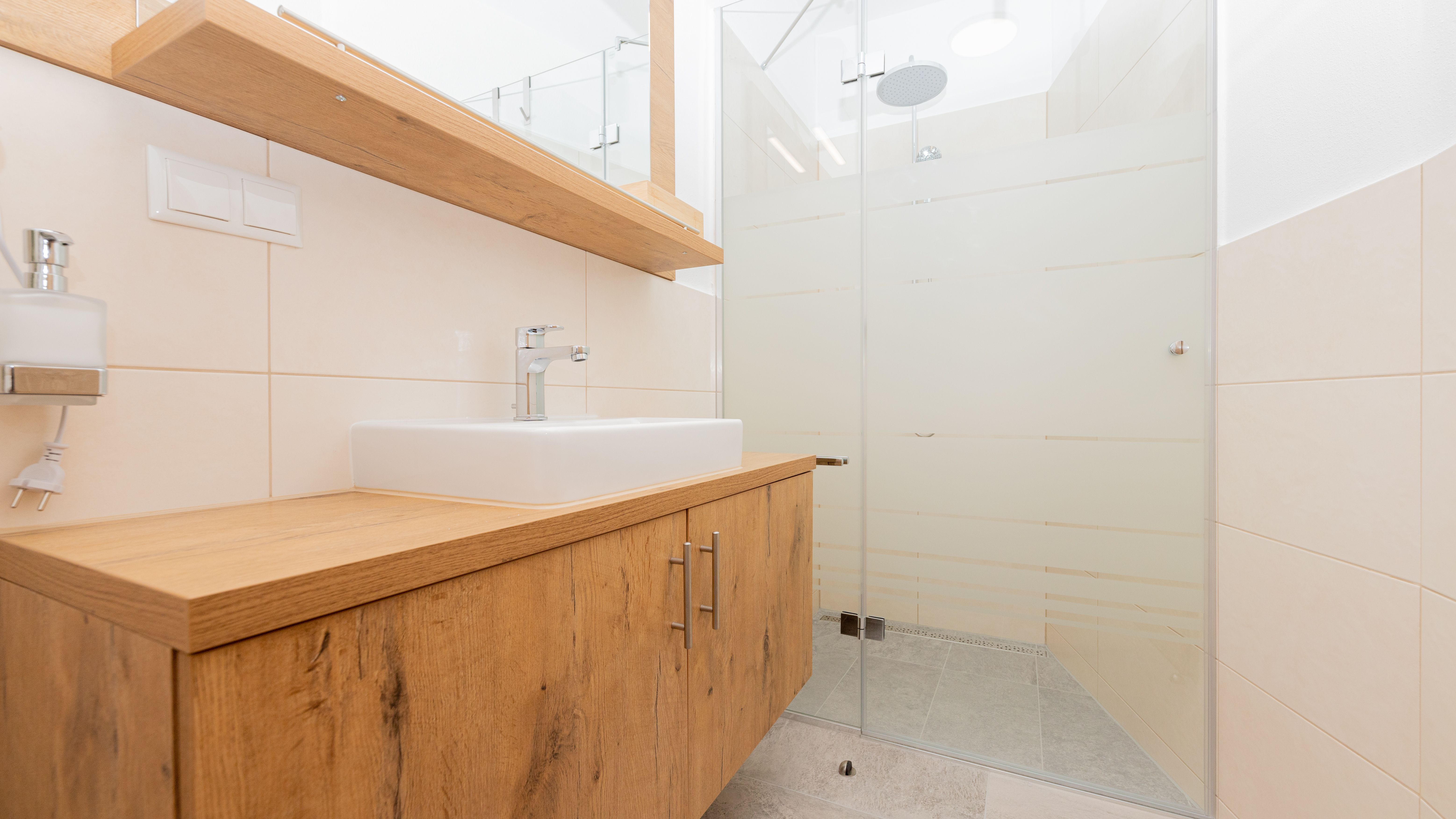 Moderní koupelna s dřevěným umyvadlem a skleněným sprchovým koutem.