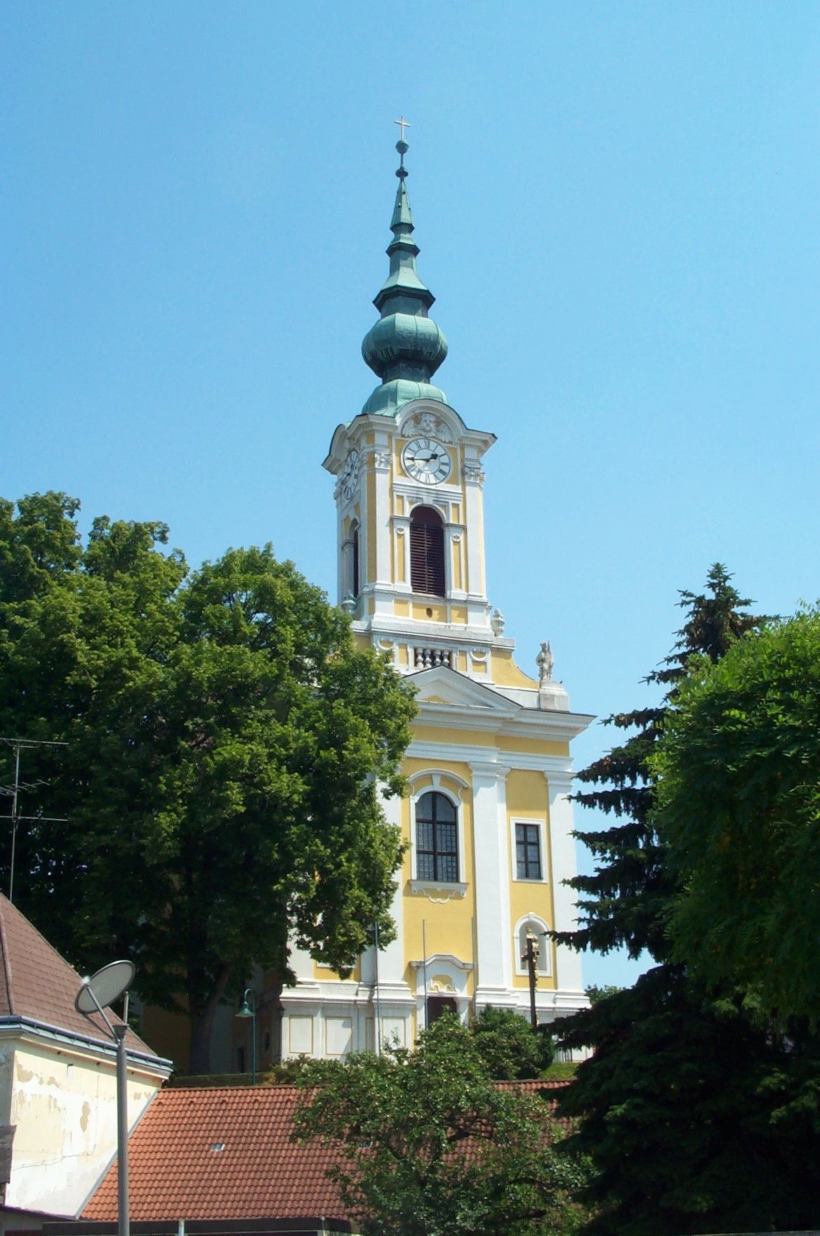 Žlutý kostel s věží a hodinami v Groß-Siegharts, obklopený stromy.