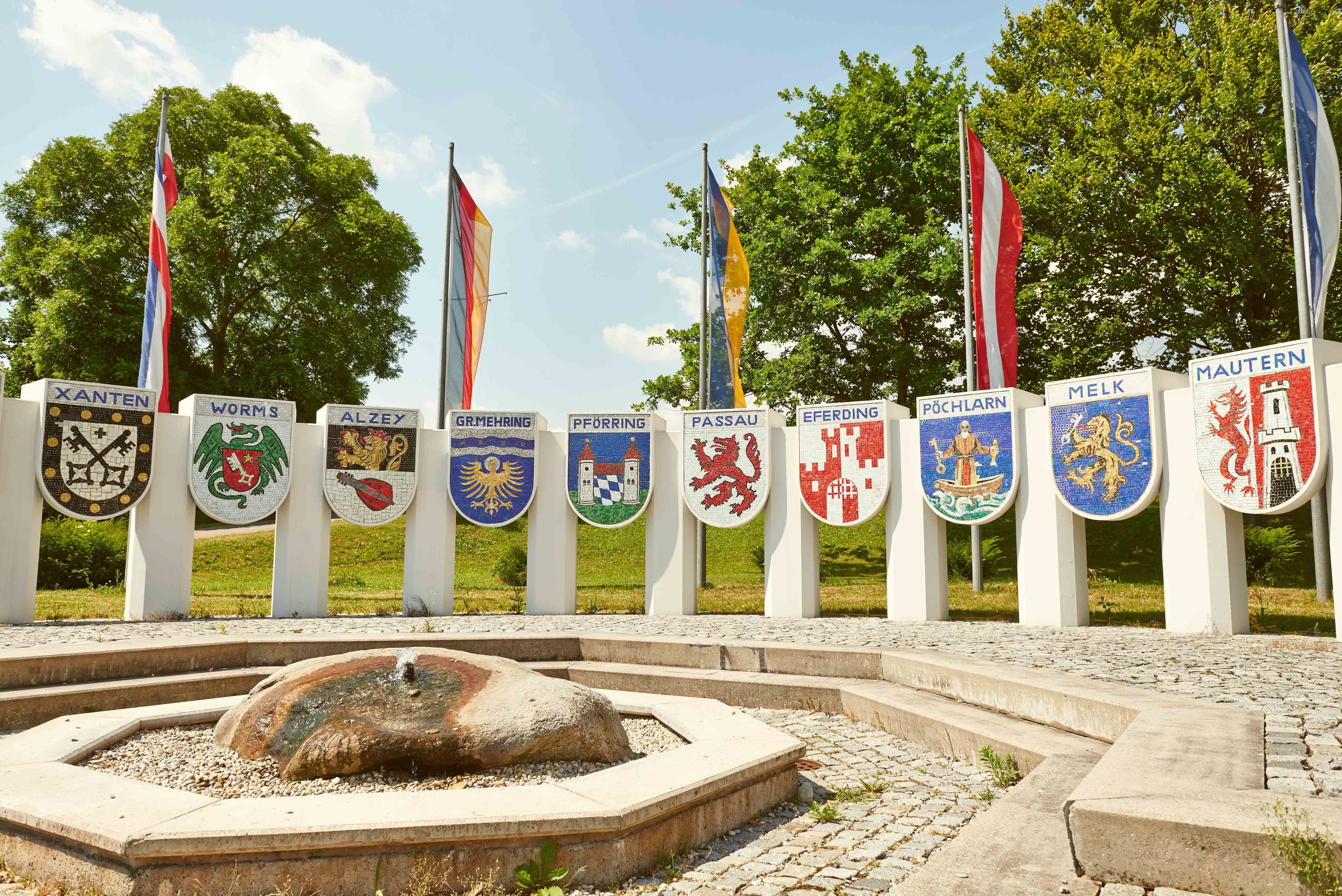 Pomník Nibelungů s erby různých měst a vlajkami v pozadí.