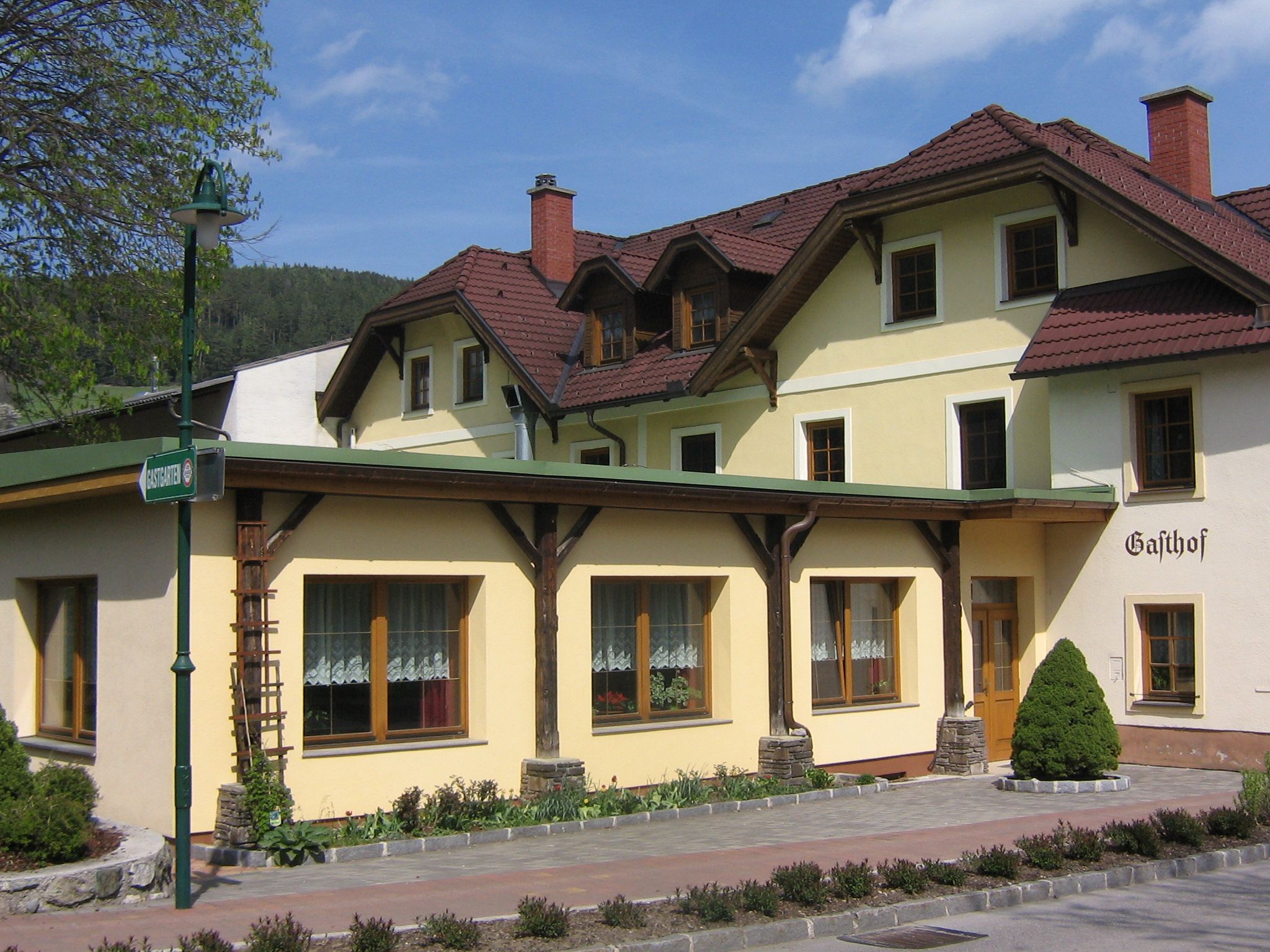 Tradiční hostinec se žlutou fasádou a červenými střešními taškami.
