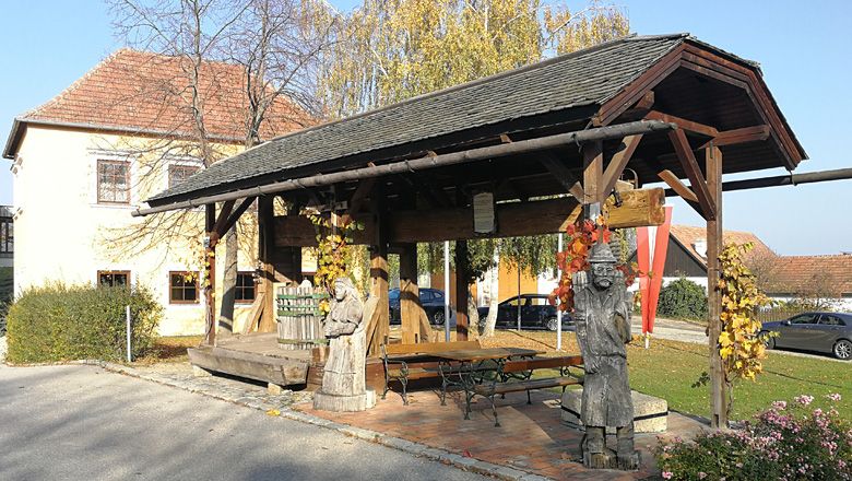 Historický lis na stromy s dřevěnými figurkami v Droßu, obklopený podzimní vegetací.