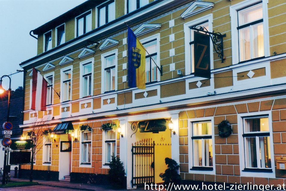 Pohled na exteriér hotelu Zierlinger se žlutou fasádou a vlajkami.