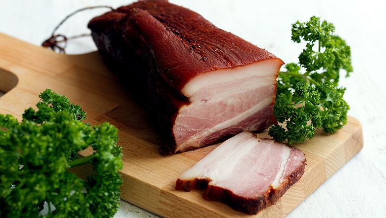 Kousek slaniny na dřevěném prkénku s petrželkou.