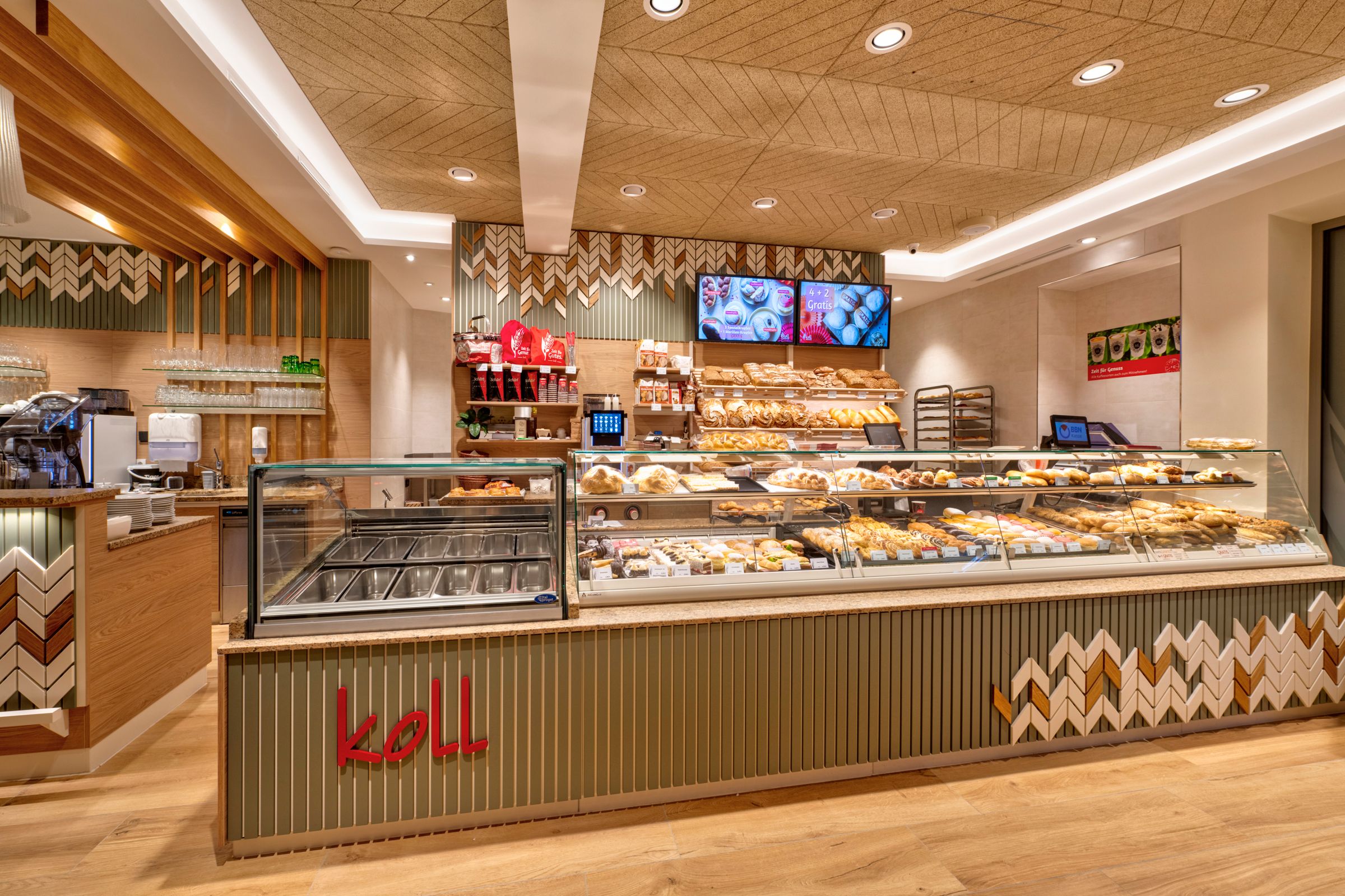 Pohled do interiéru moderní pekárny s pultem plným pečiva a kávovarem.