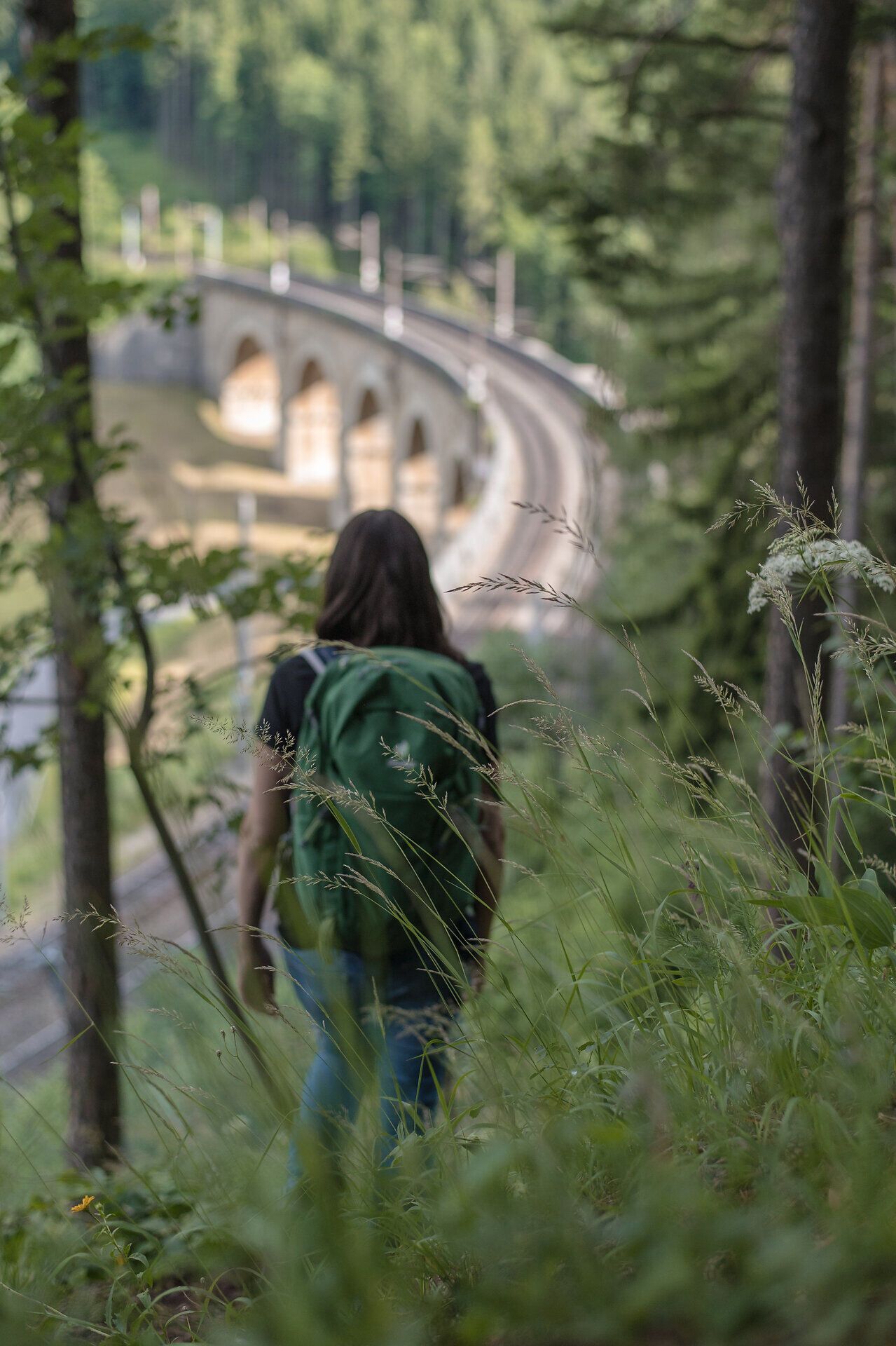 Turista si vychutnává čerstvý horský vzduch a úchvatný výhled na kopce a zakřivenou železniční trať, která se elegantně vine krajinou. Toto místo obklopené svěží zelení a jemným šuměním přírody zve k odpočinku a poznávání krás Vídeňských Alp v Dolním Rakousku.