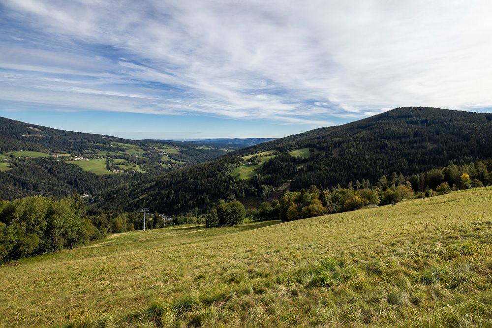 Rozlehlá zelená krajina s kopci a lesy pod zataženou oblohou.