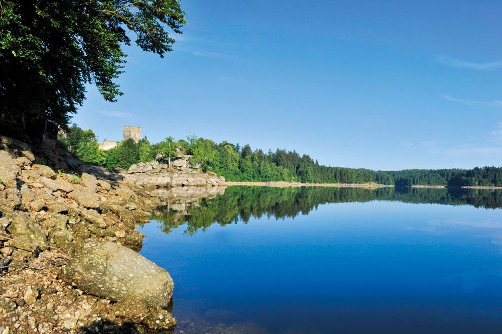 Kampsee Ottenstein s klidnou vodou, zalesněnými břehy a hradem v pozadí.
