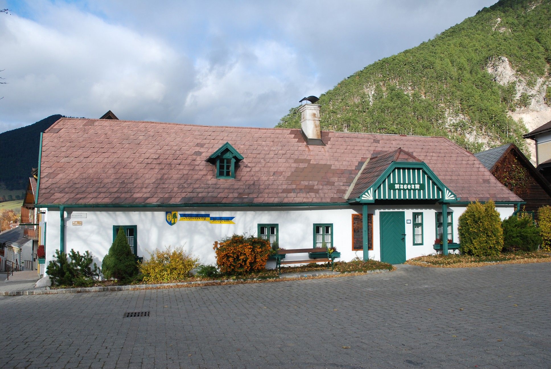 Schneeberg Museum Puchberg, tradiční budova se zelenou střechou a komínem, obklopená horami a stromy.