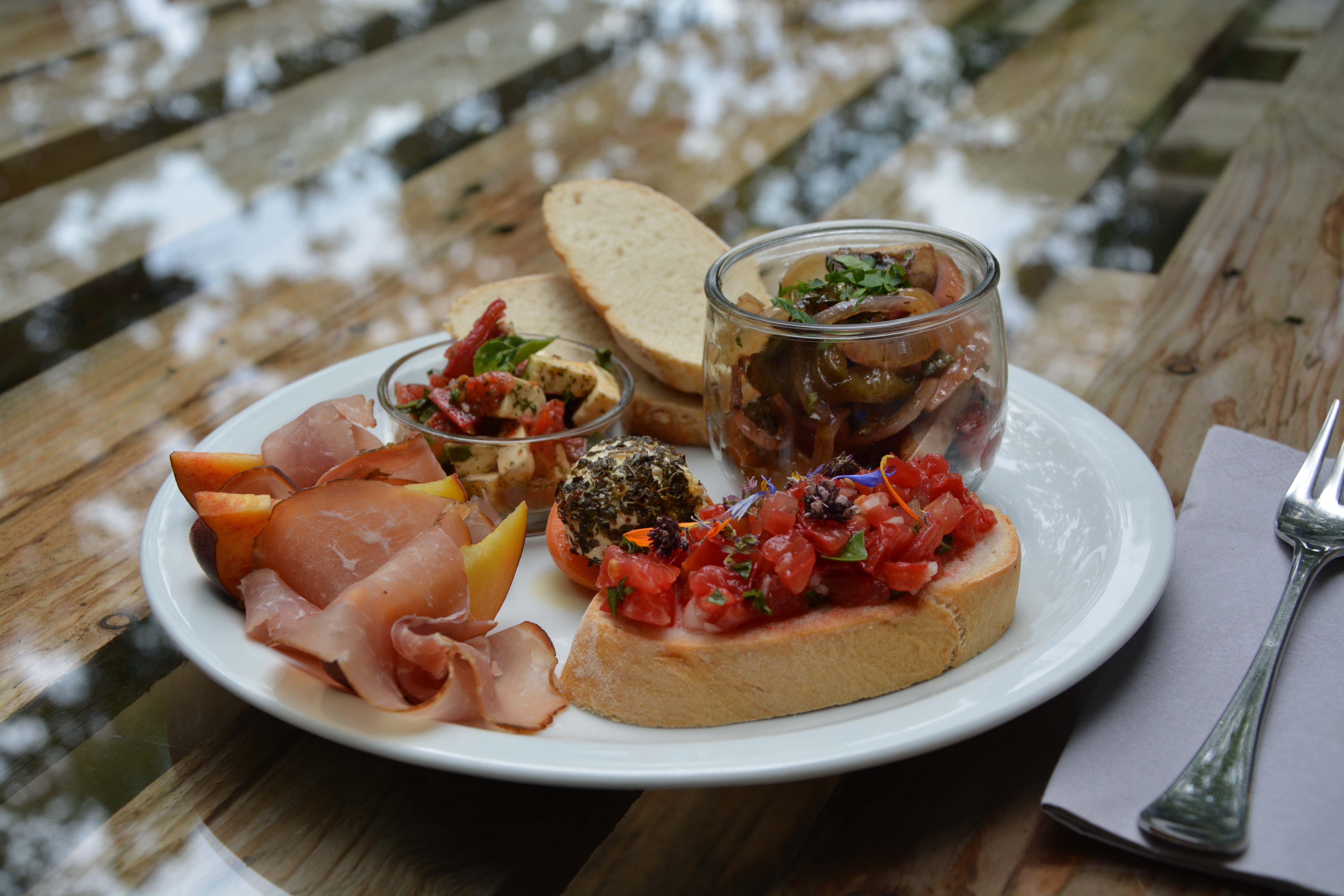 Talíř s chlebem, šunkou, antipastami, bruschetty a ovoce na dřevěném stole.