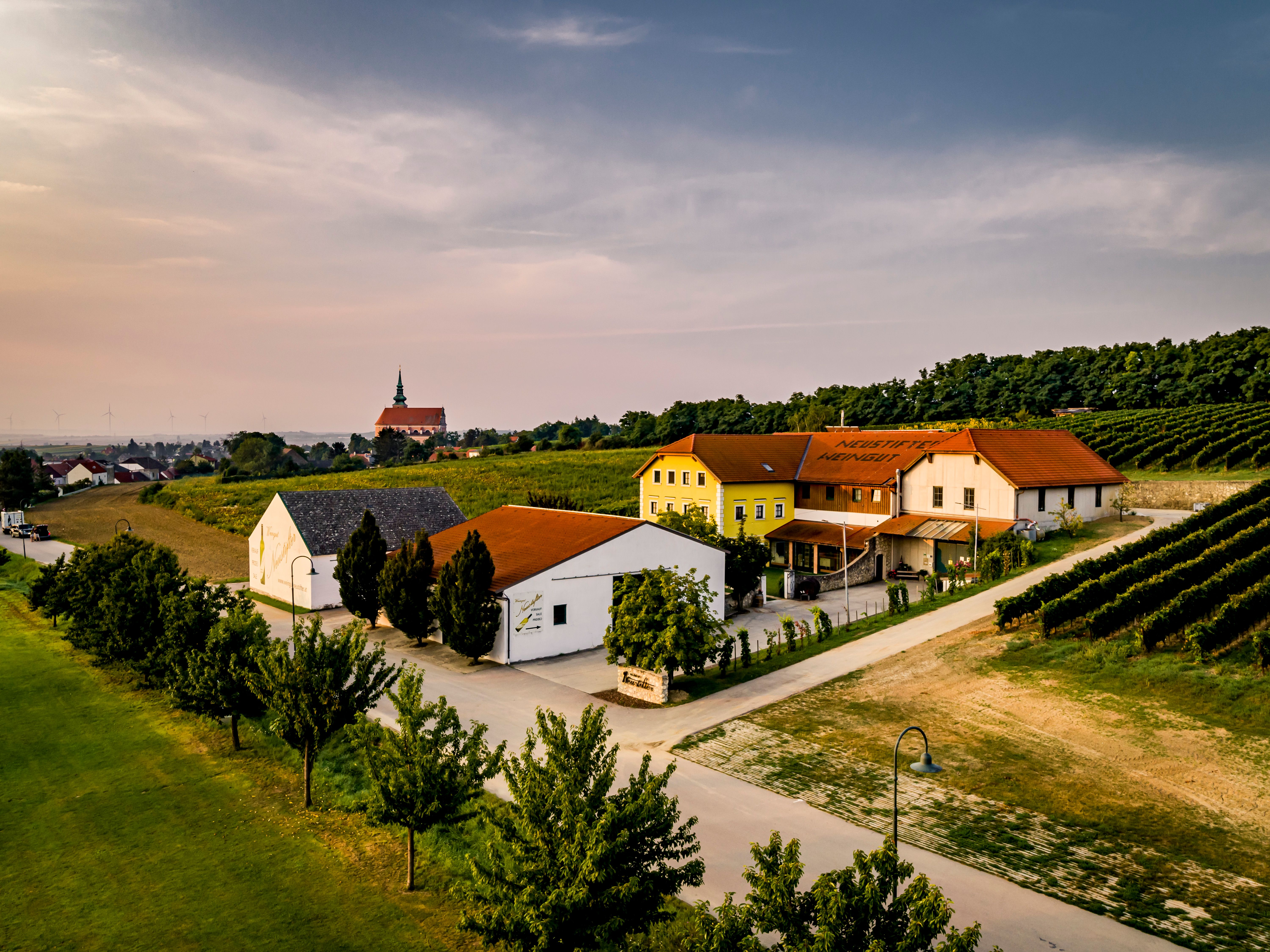 Letecký pohled na vinařství s budovami a vinicemi při západu slunce.