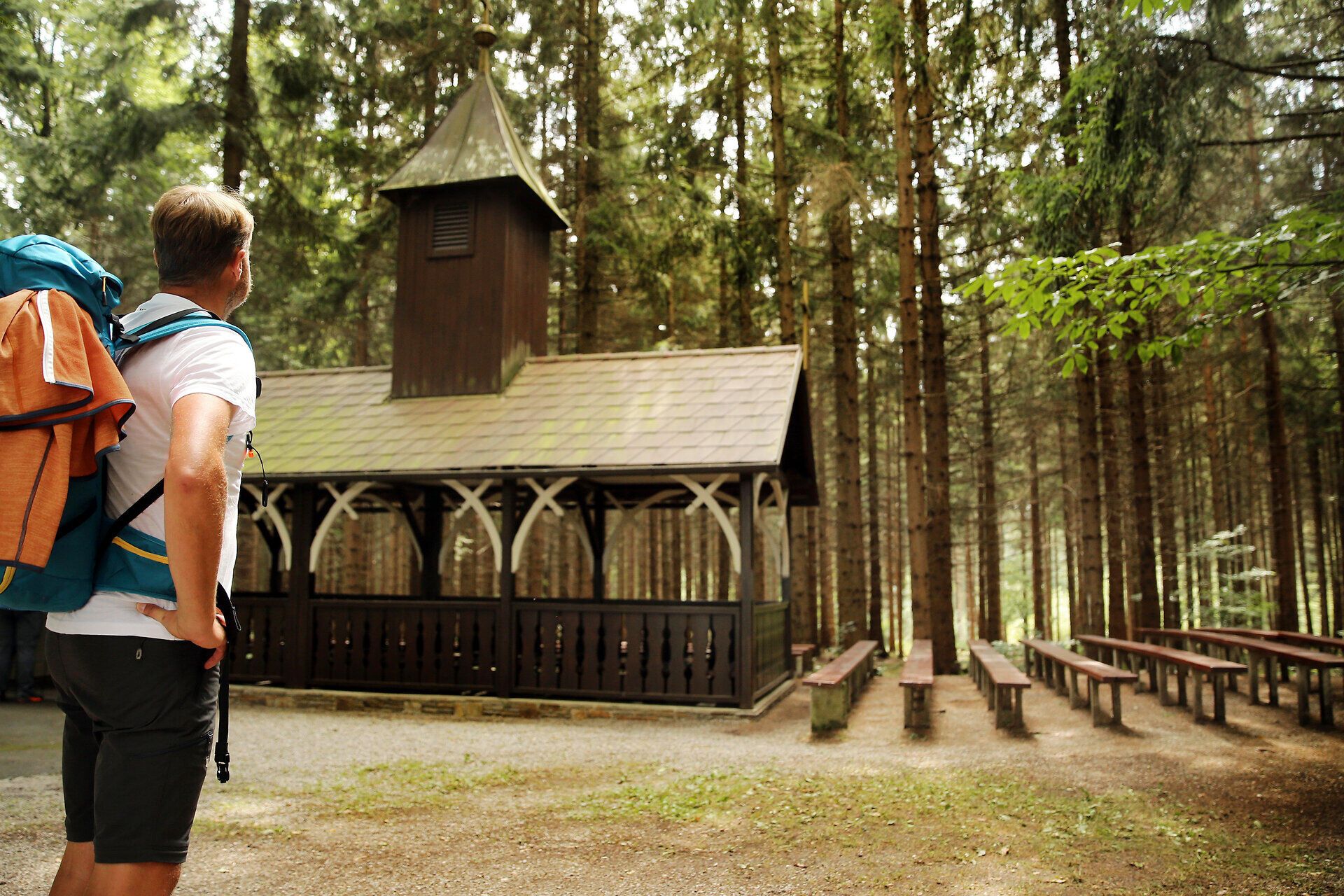 Poutník obdivuje dřevěný kostel uprostřed lesa.