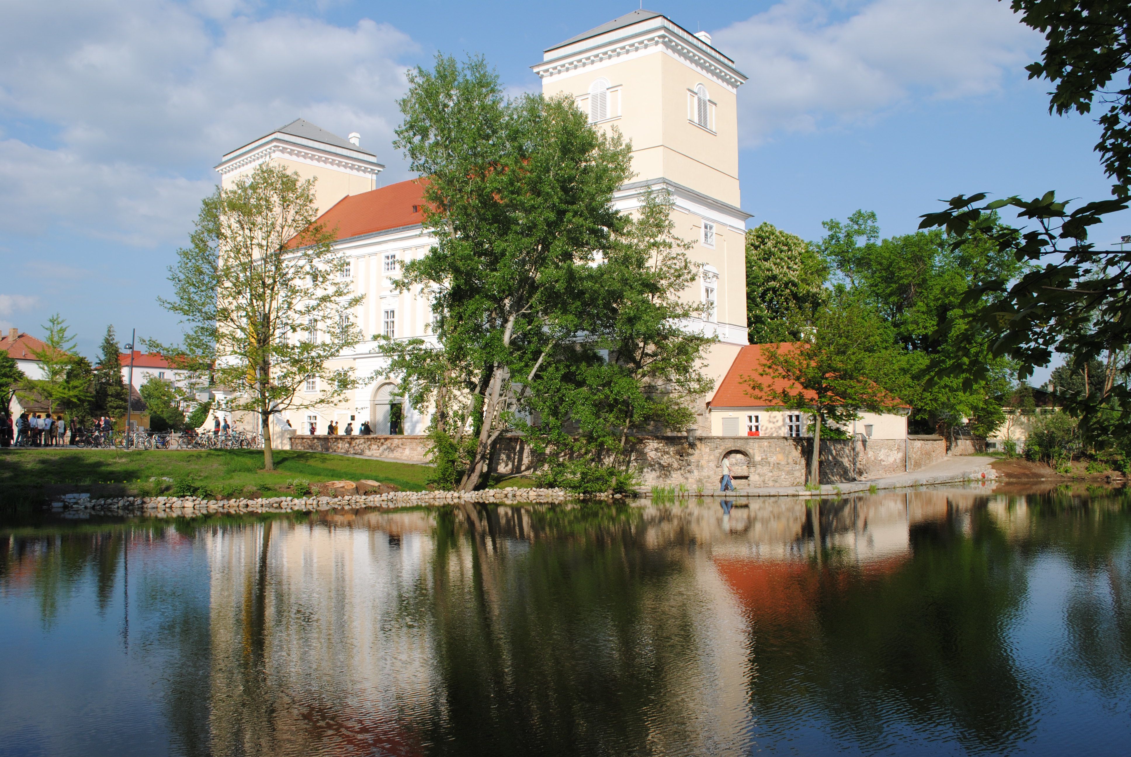 Zámek Wolkersdorf s odrazem ve vodě a obklopený stromy.