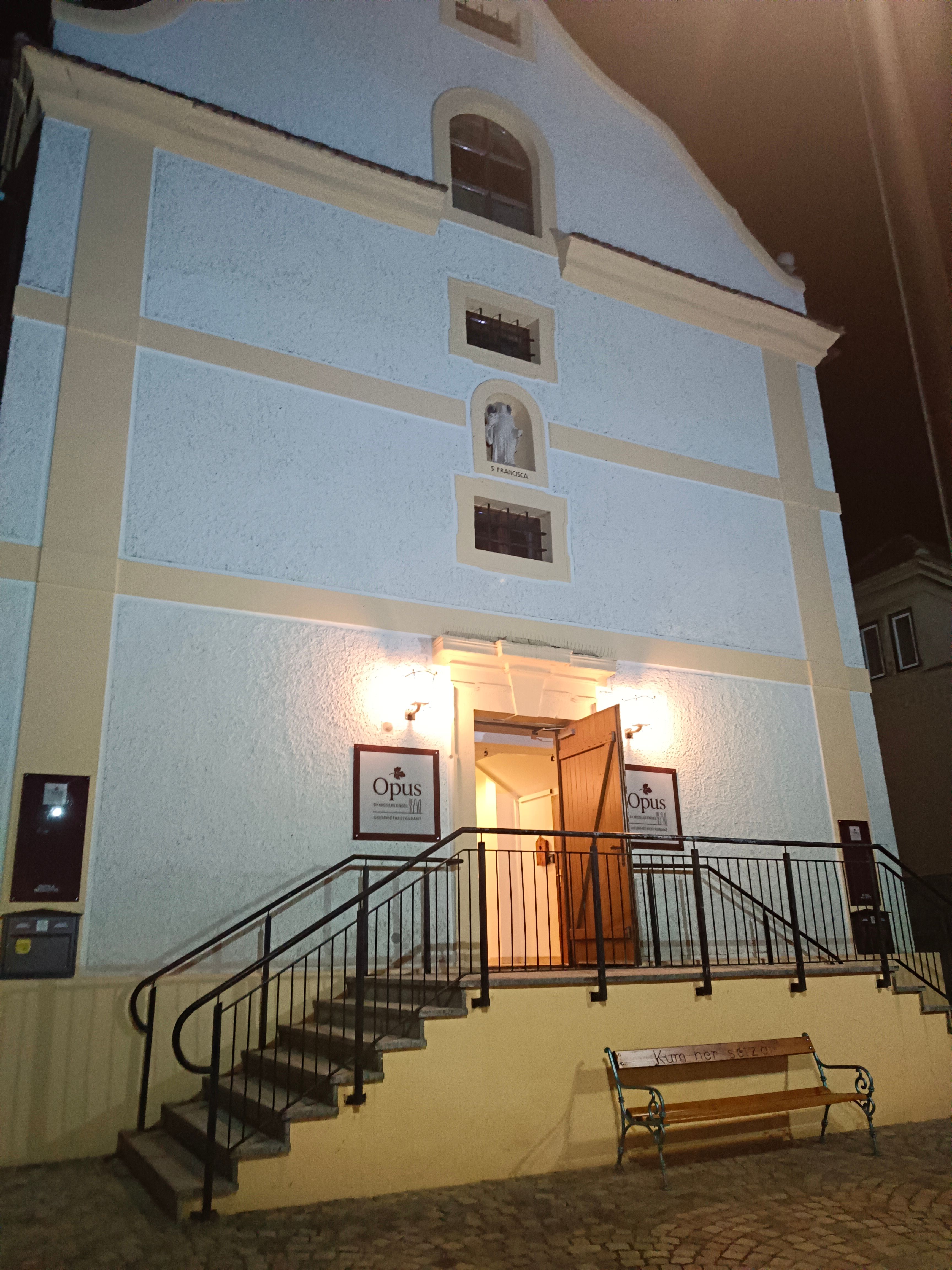 Vchod do budovy se schody a otevřenými dveřmi, osvětlený v noci.