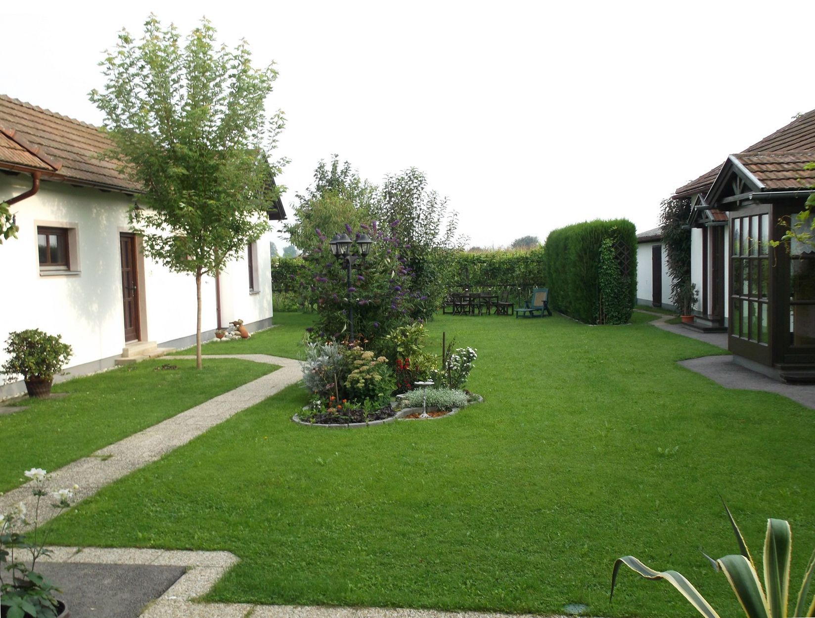 Velmi dobře udržovaná zahrada s výhledem na keře a stromy, s částí budovy v pozadí.