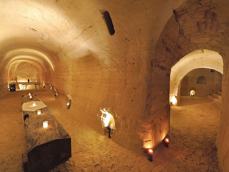 Podzemní pískovcový sklep se svíčkami a rustikálními stoly.