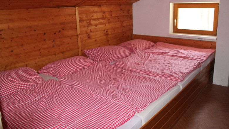 Tři postele s červenobílými kostkovanými peřinami v pokoji obloženém dřevem.