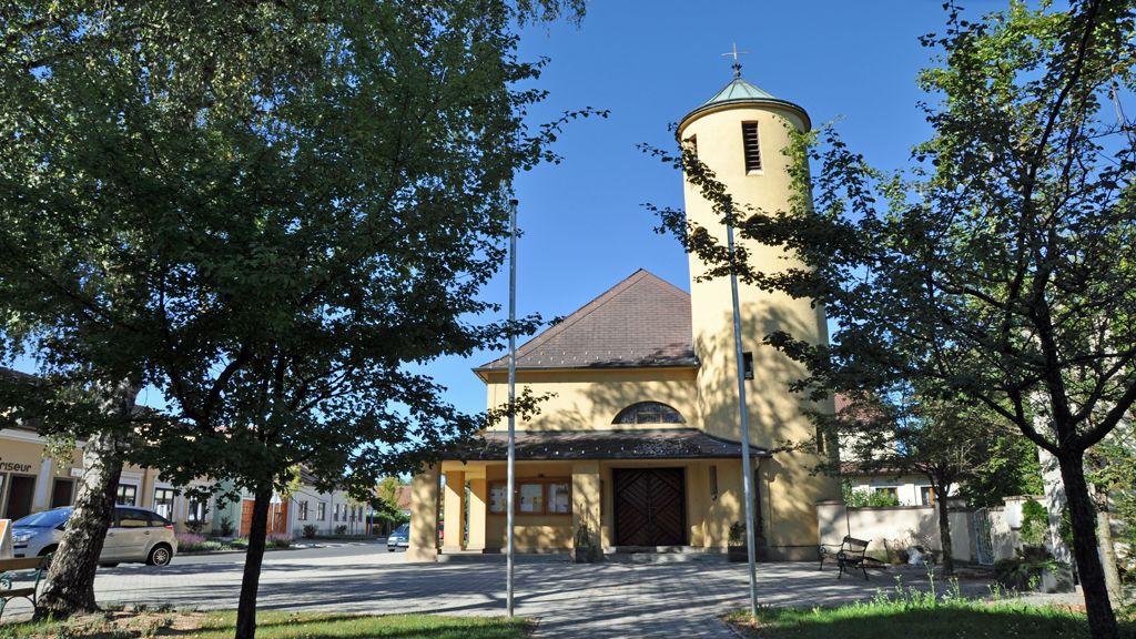 Kostel svatého Antonína v Bad Erlachu se žlutou věží a stromy v popředí.
