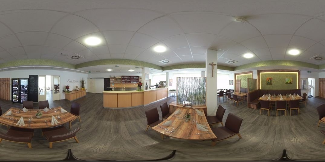 Pohled do interiéru moderní restaurace s dřevěnými stoly a židlemi, zdobené rostlinami a uměleckými díly na stěnách.