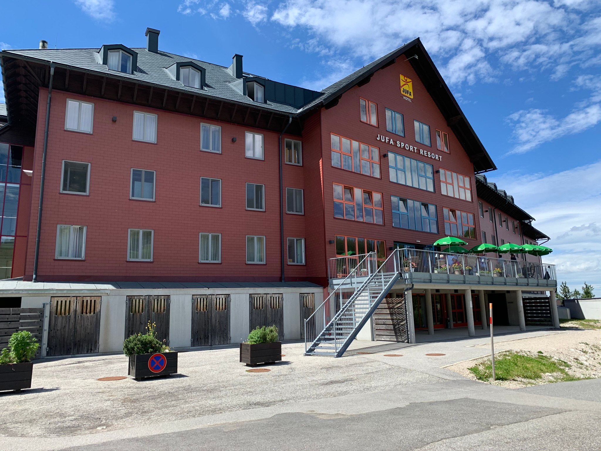 JUFA Sport Resort Hochkar s červenou fasádou a terasou se zelenými slunečníky.