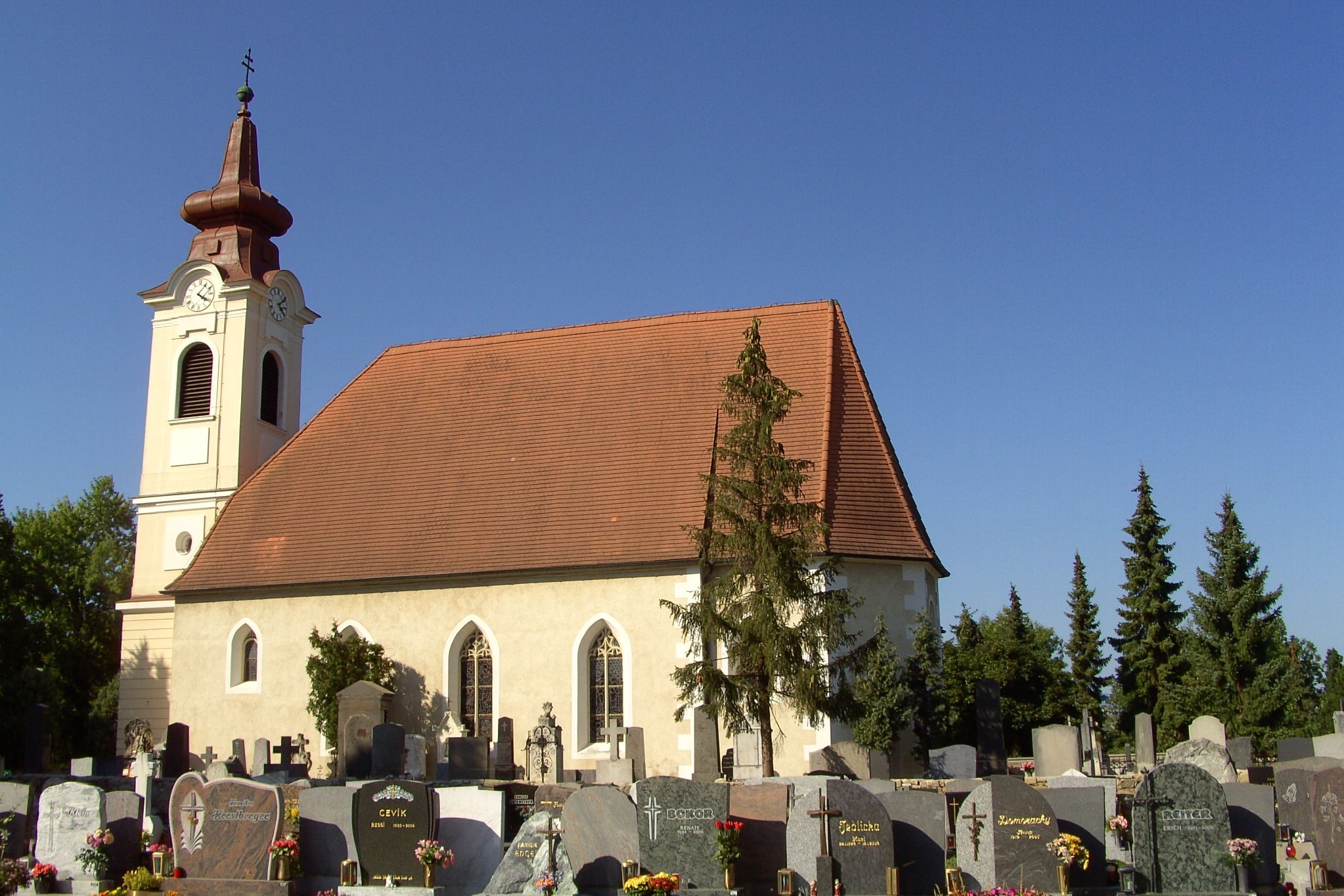 Pohled na kostel v exteriéru s hřbitovem v popředí a modrou oblohou.