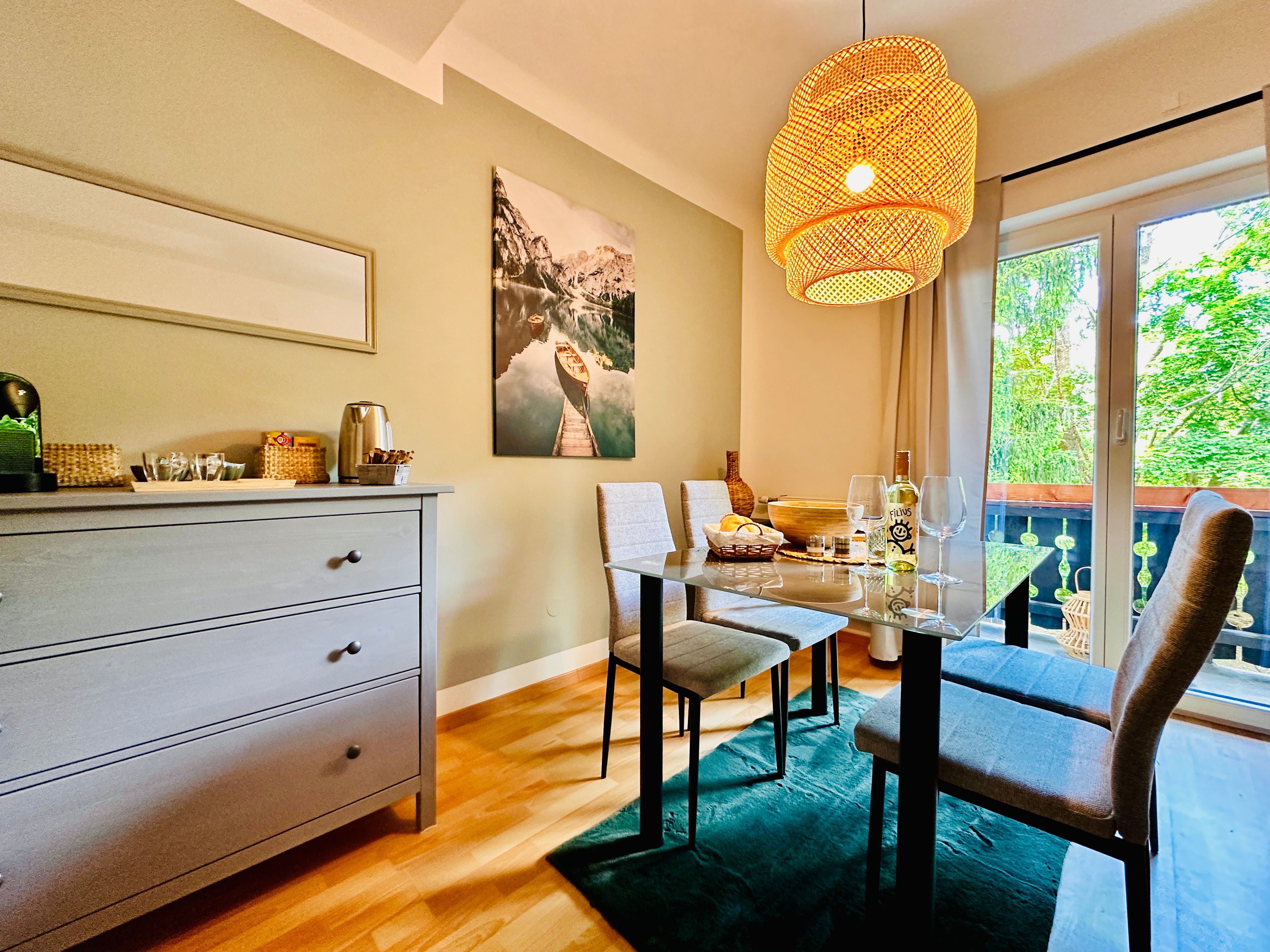 Útulná jídelna se stolem, židlemi a závěsnou lampou, výhled na balkon a přírodu.