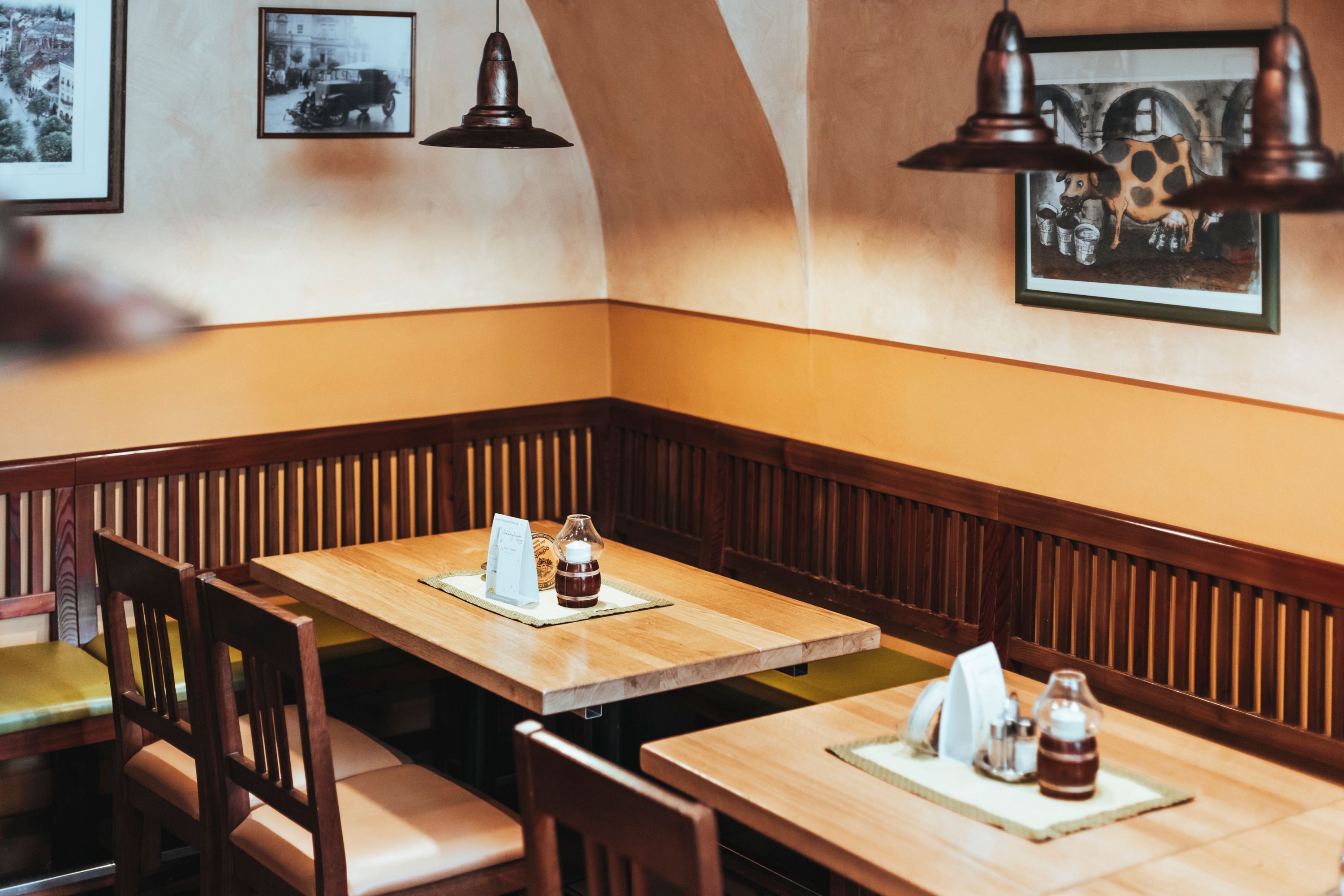 Útulné posezení v restauraci s dřevěnými stoly a židlemi, zdobené obrázky na stěnách.