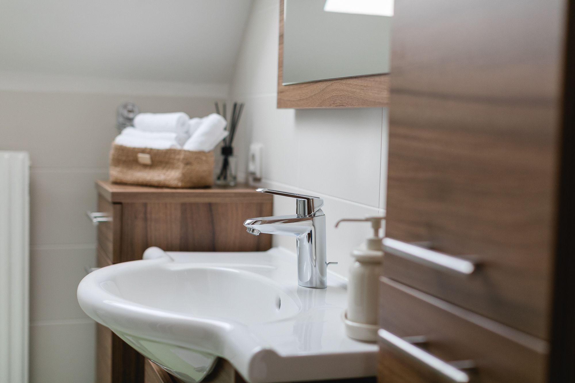 Moderní koupelna s umyvadlem, dřevěnými skříňkami a ručníky v koši.