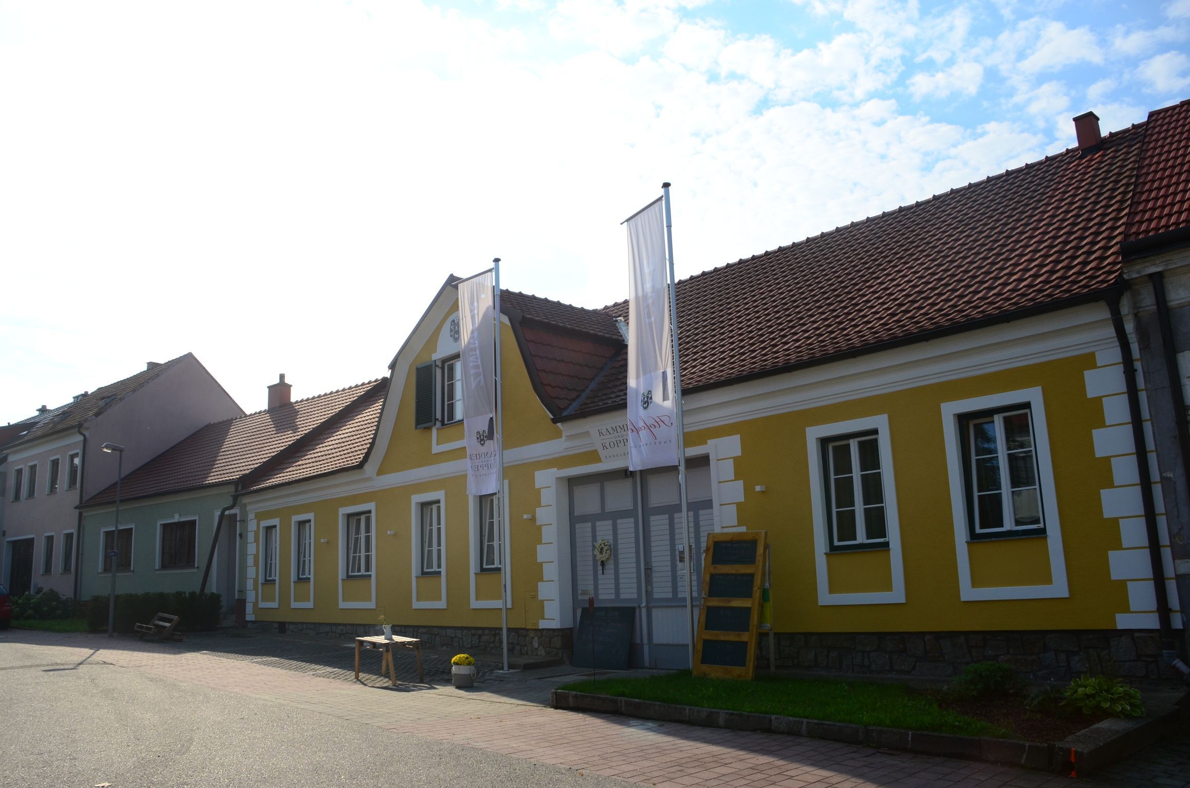 Žlutá budova s červenými střešními taškami a dvěma vlajkami před ní.