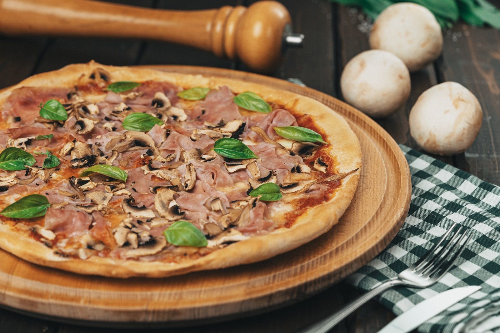 Pizza se šunkou, žampiony a bazalkou na dřevěném prkénku.