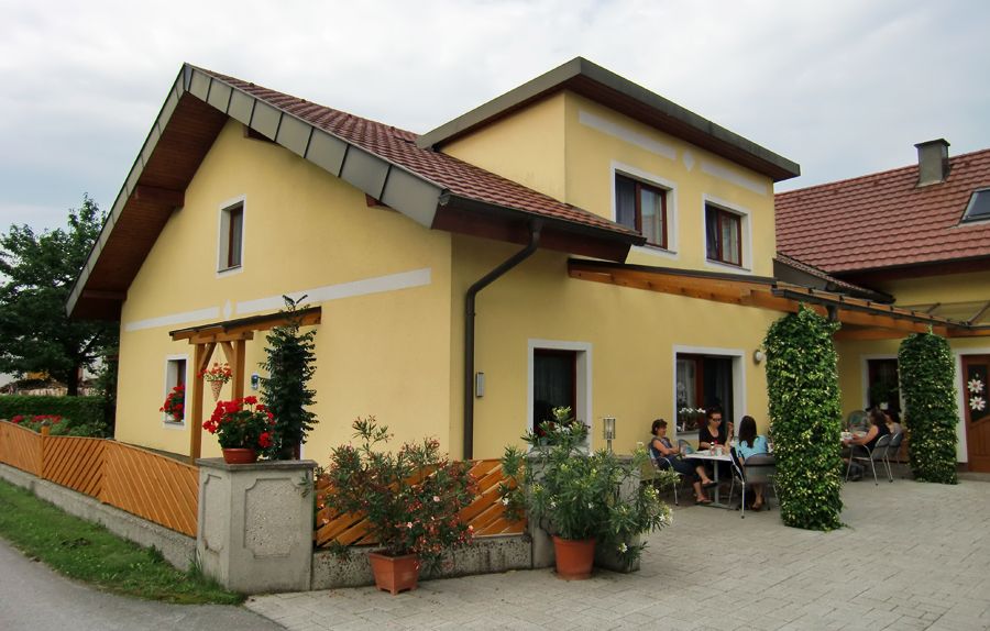 Žlutý dům s terasou a lidmi sedícími venku.