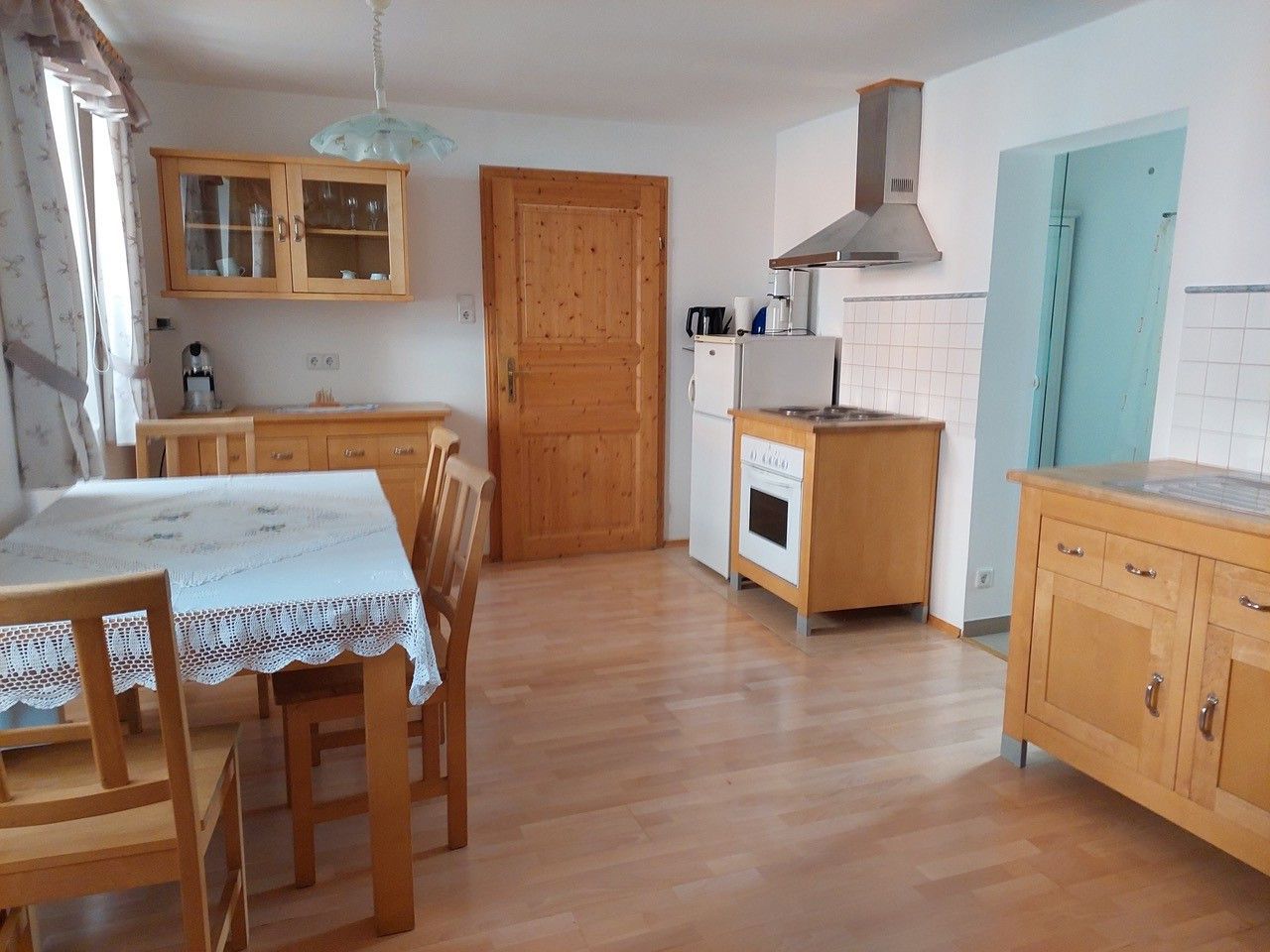 Kuchyň-obývací pokoj s dřevěným nábytkem, jídelním stolem, židlemi, sporákem, lednicí a nástěnnou skříní.