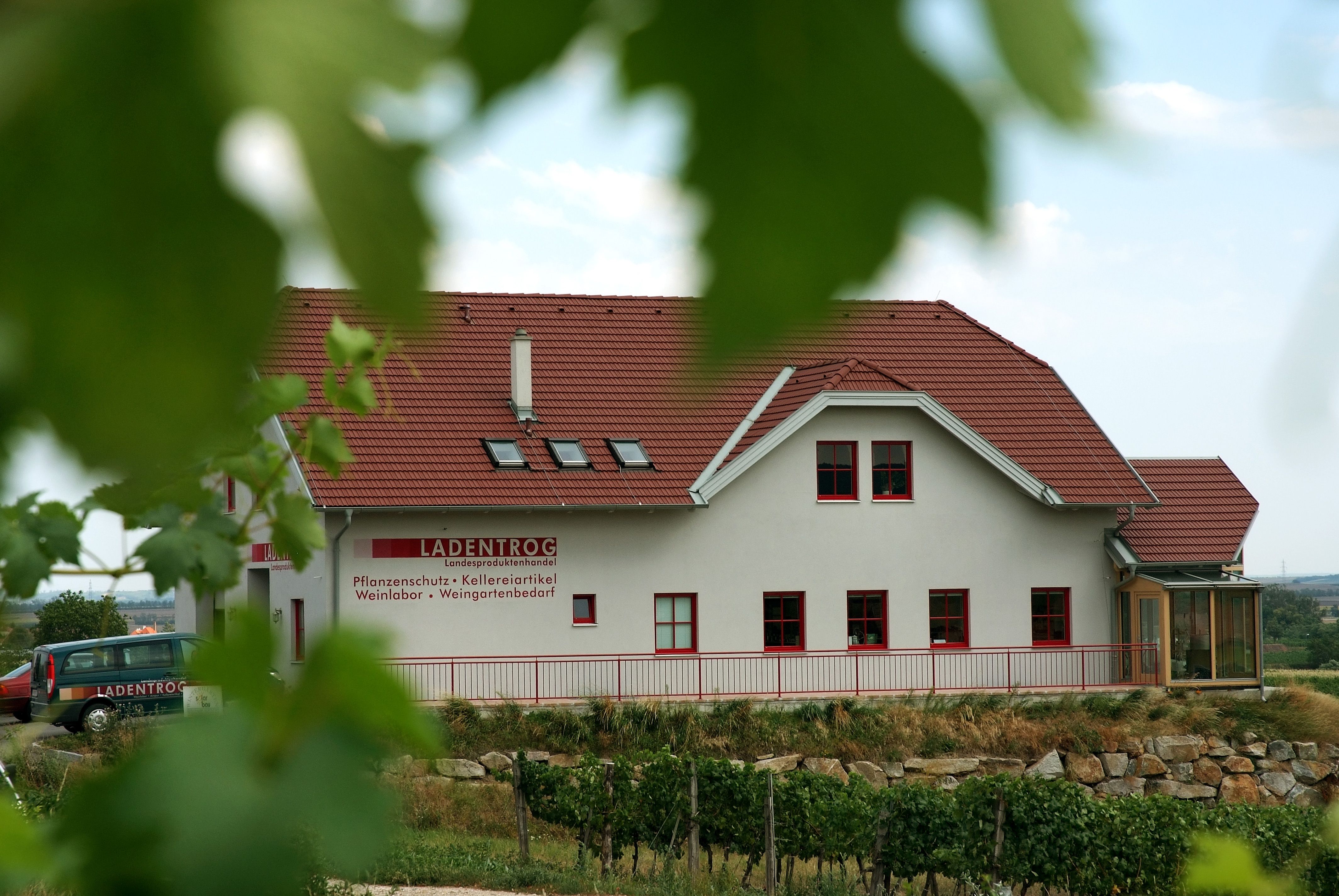 Budova s červenou střechou a nápisem "LADENTROG" ve venkovském prostředí.