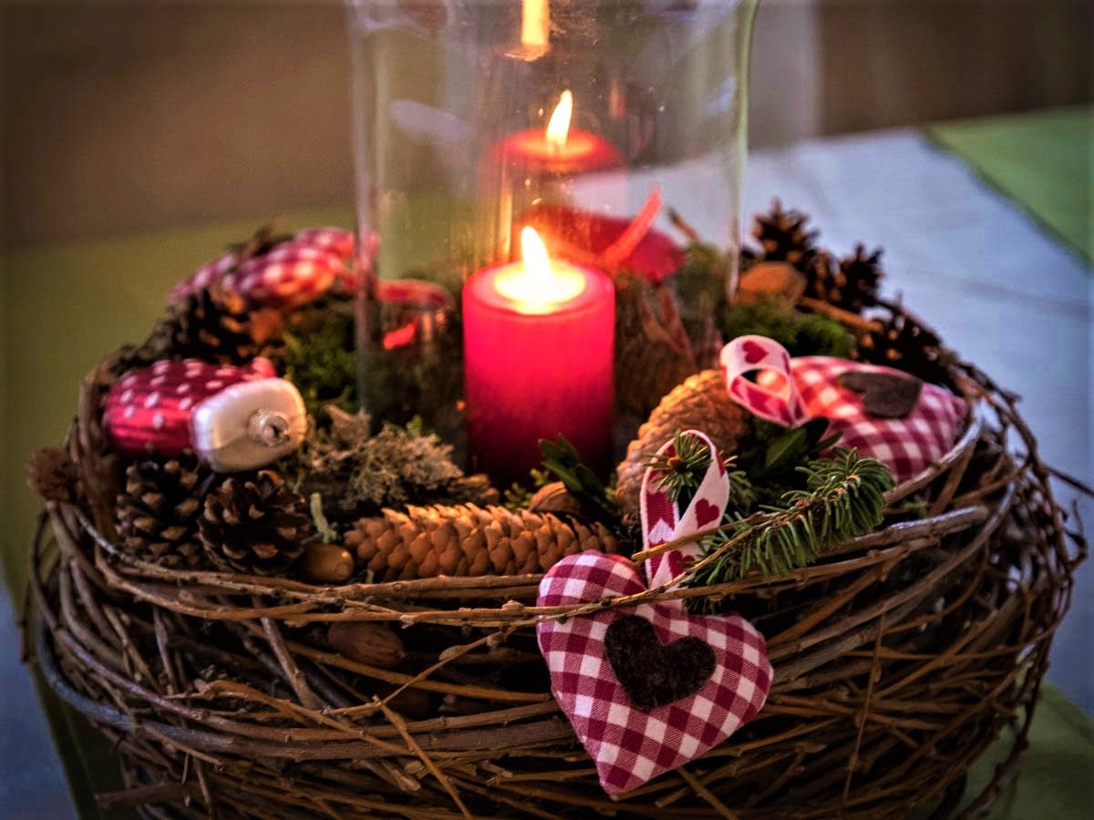 Adventní věnec s hořící červenou svíčkou, borovými šiškami a červenobílými kostkovanými látkovými srdíčky.