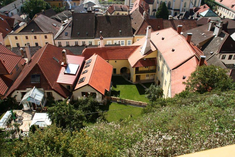 Letecký pohled na domy s červenými střechami a zeleným vnitřním dvorem.