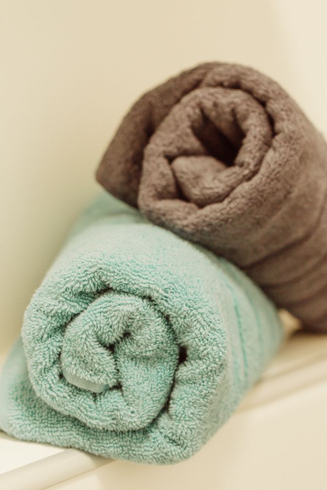 Na polici leží dva srolované ručníky, jeden tyrkysový a druhý hnědý.