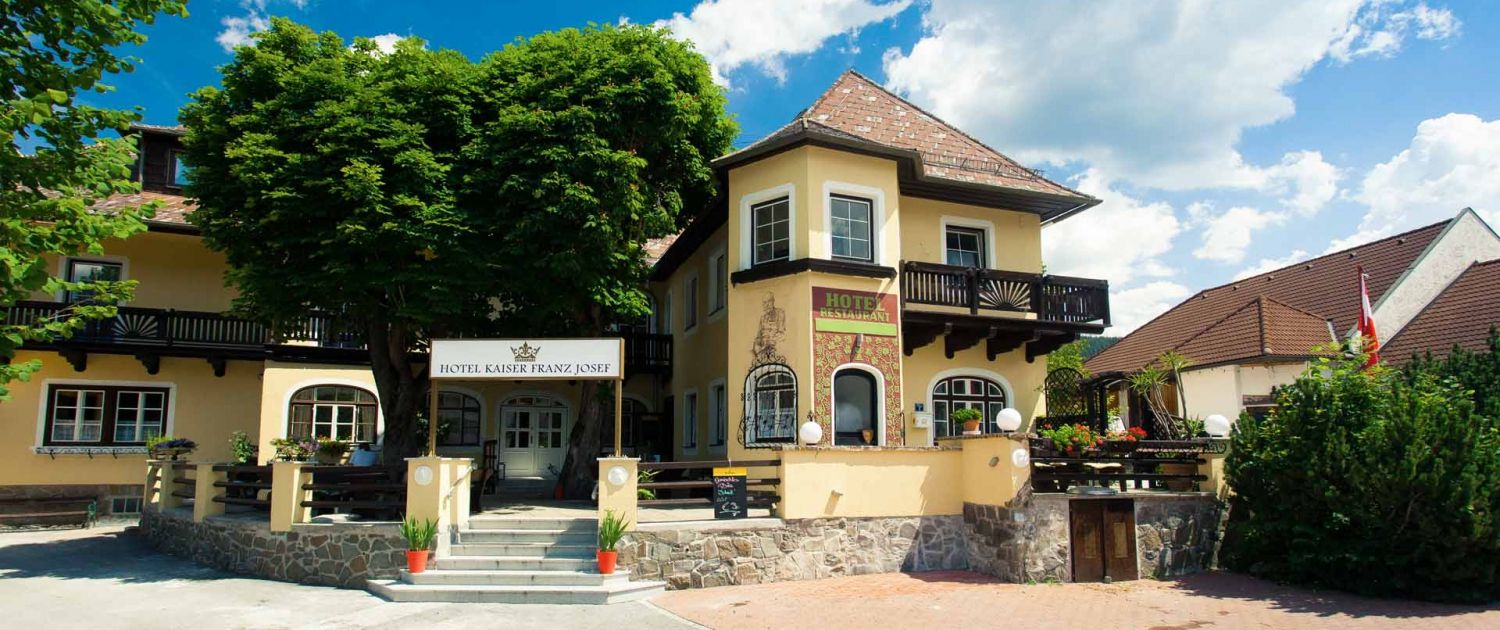 Vchod do hotelu Kaiser Franz Josef se žlutou fasádou a balkonem.