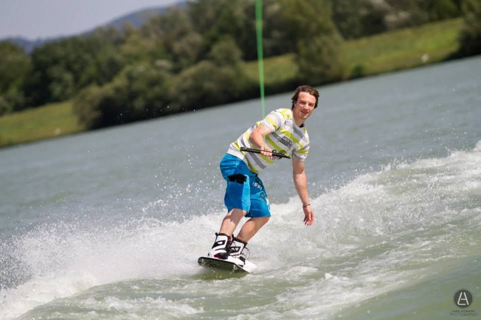 Wakeboardista jezdí na jezeře obklopeném zelenou krajinou.
