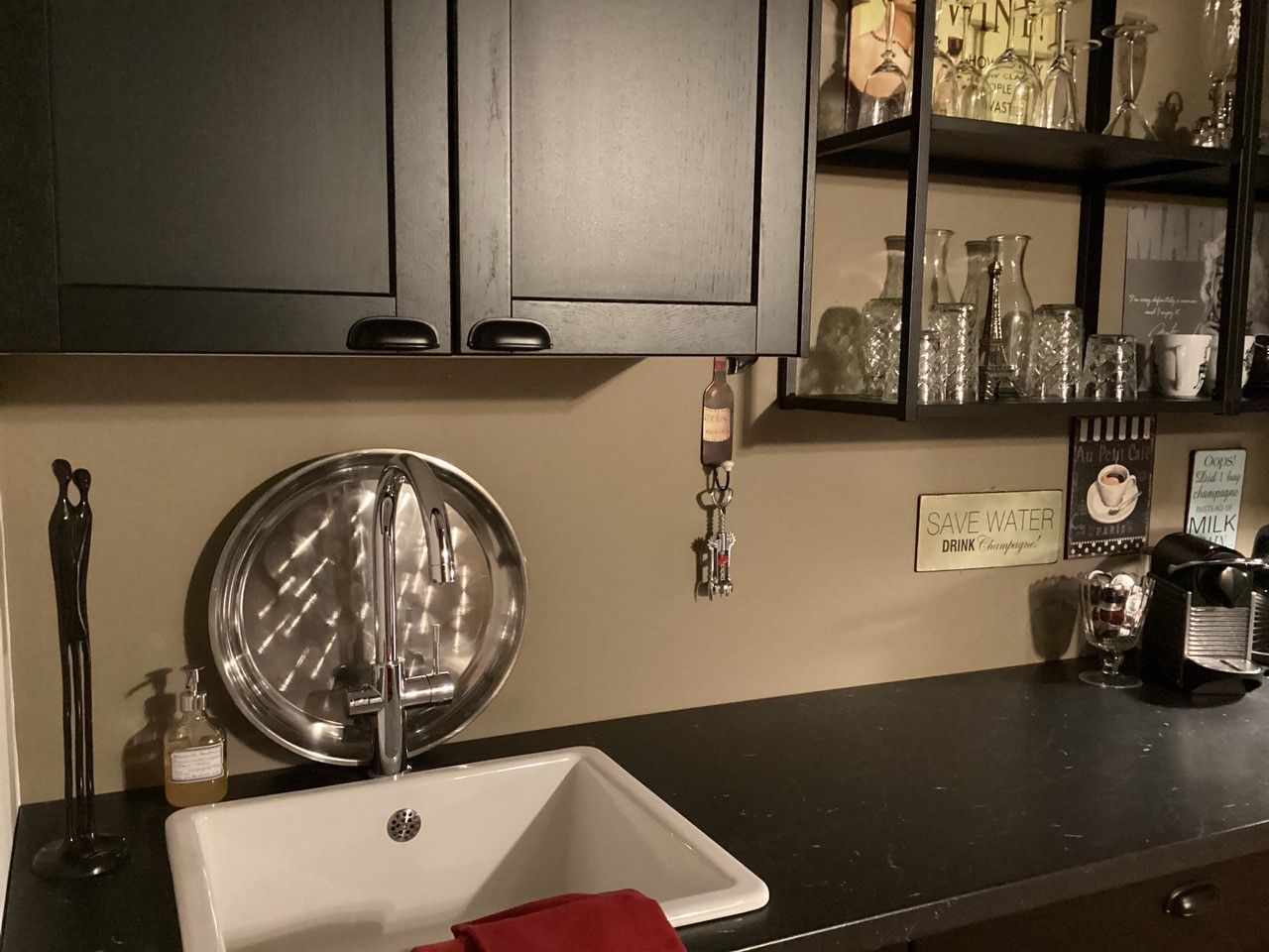 Moderní kuchyňský kout s dřezem, černou skříňkou, policemi se sklenicemi a kávovarem.