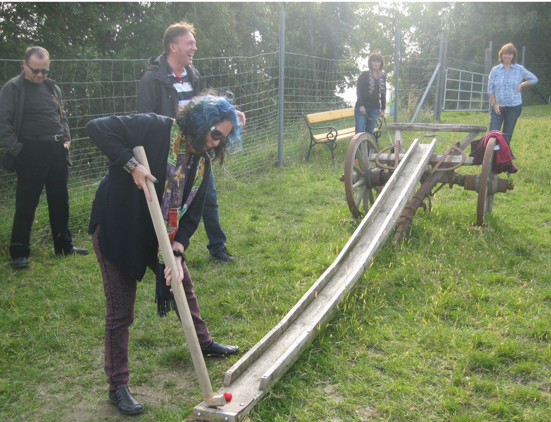 Osoba hraje farmářský golf s dřevěnou holí na louce.