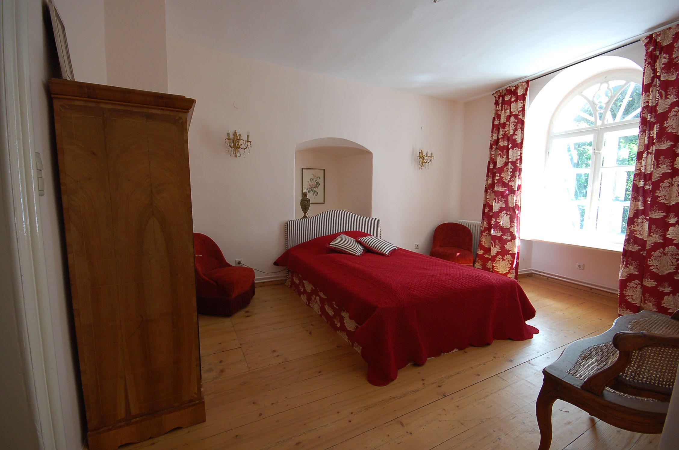 Útulná ložnice s červenou postelí, červenými závěsy a dřevěným nábytkem.