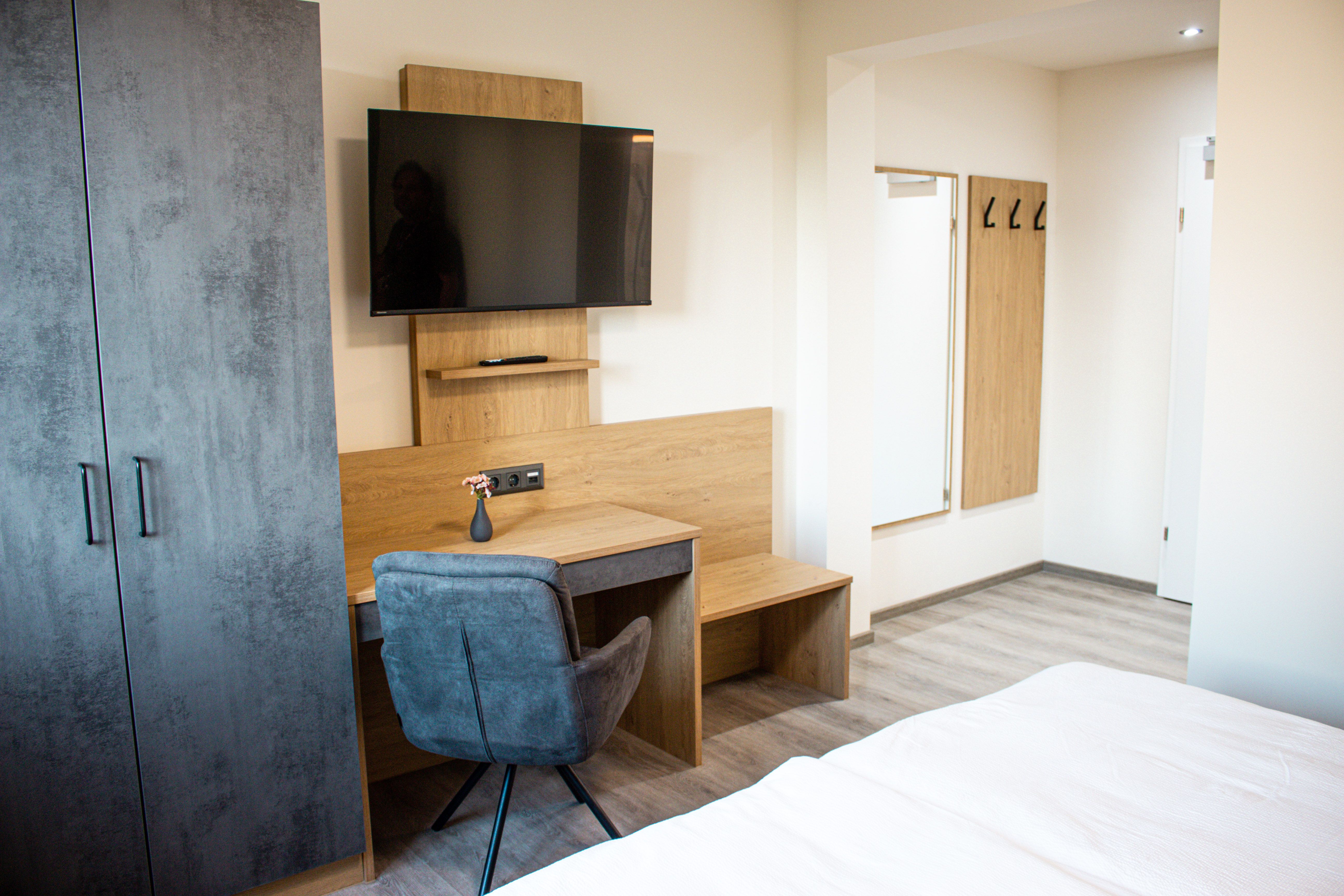 Moderně zařízený hotelový pokoj se psacím stolem, TV, šatní skříní a zrcadlem.