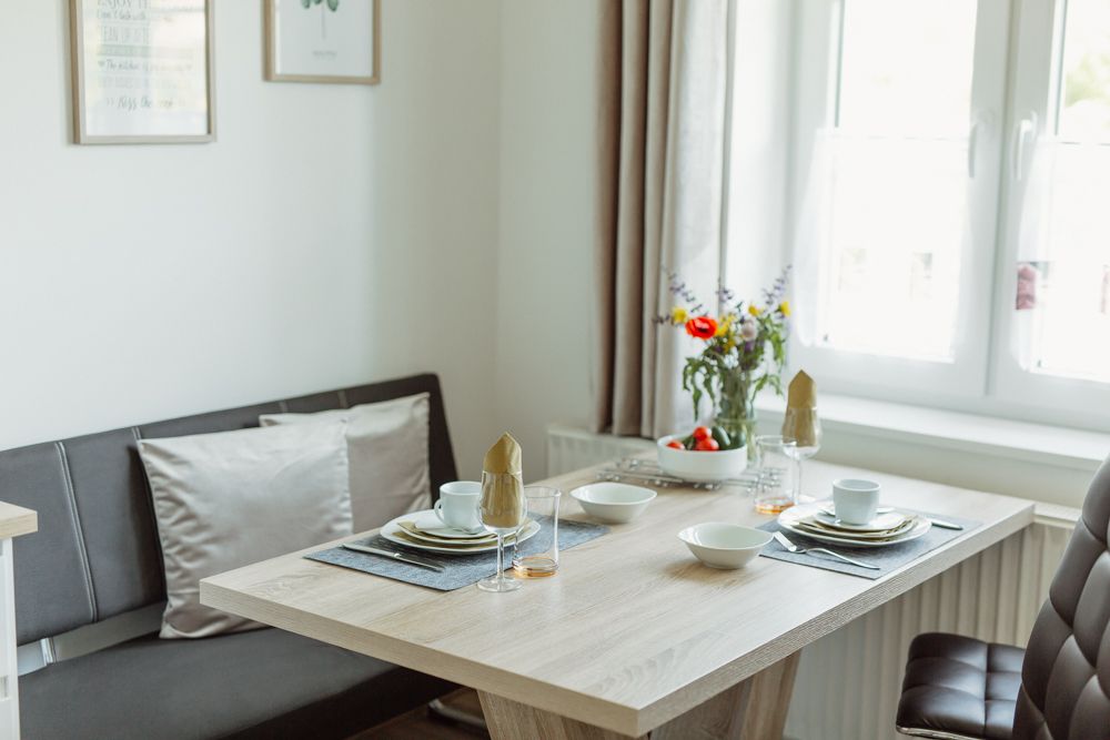 Jídelní kout v moderním bytě s prostíráním a květinami.